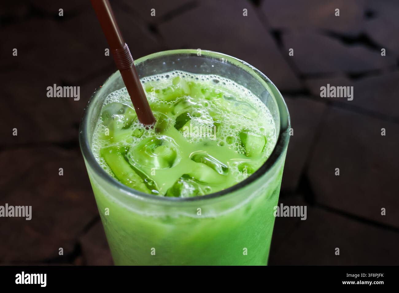 Una bevanda matcha verde ghiacciata con cannuccia e schiuma frizzante in un bicchiere trasparente, bevanda fredda rinfrescante servita con ghiaccio per il piacere estivo Foto Stock
