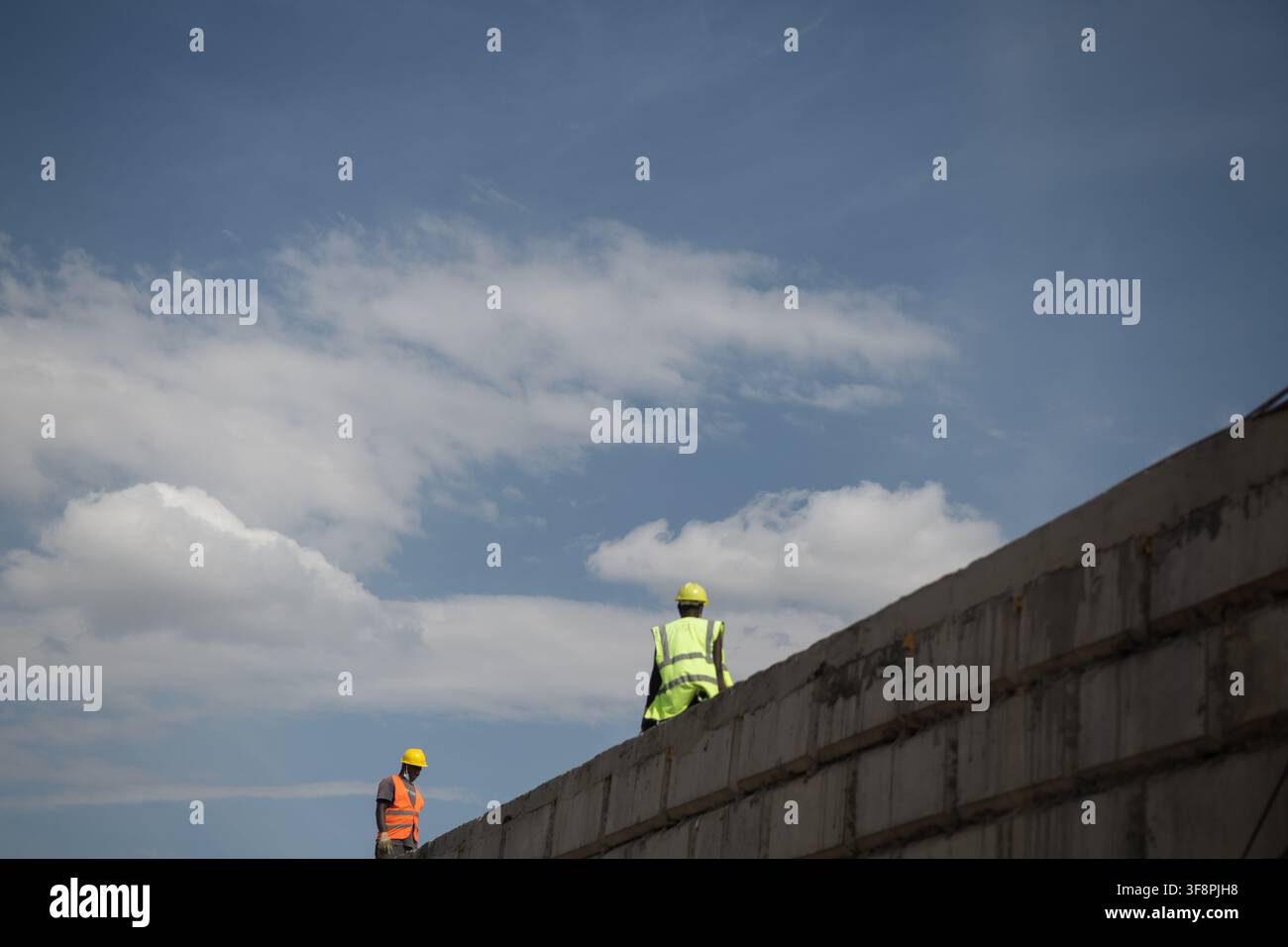 Nairobi, Kenya - 06 febbraio 2022: Vista di due operai edili che indossano giubbotti ad alta visibilità e caschi gialli in piedi su un muro di cemento e Foto Stock