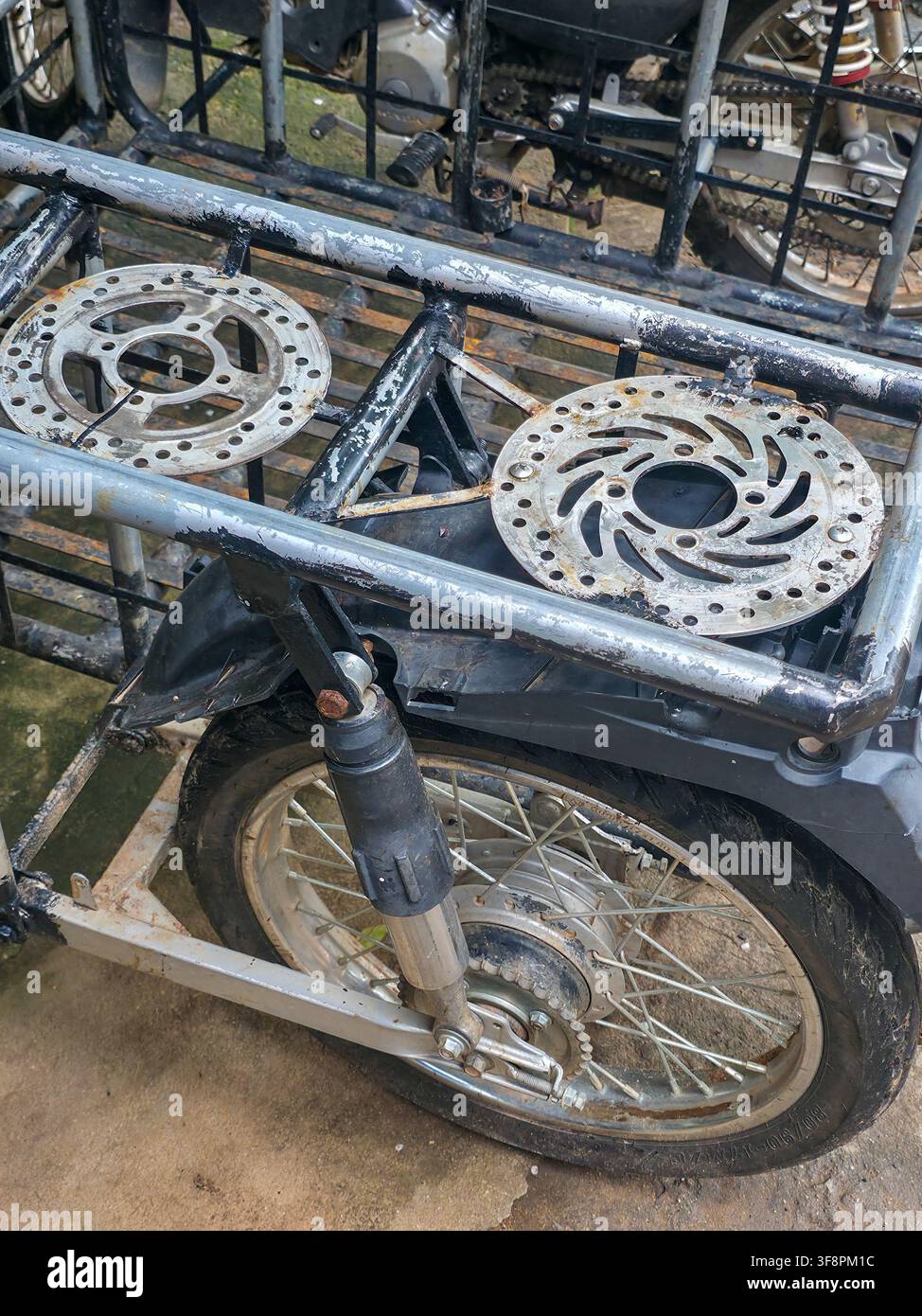 Una ruota di moto arrugginita e un telaio di carico in metallo con dischi dei freni consumati e vernice scrostata che mostra un decadimento industriale grezzo e un'atmosfera esterna sottile Foto Stock