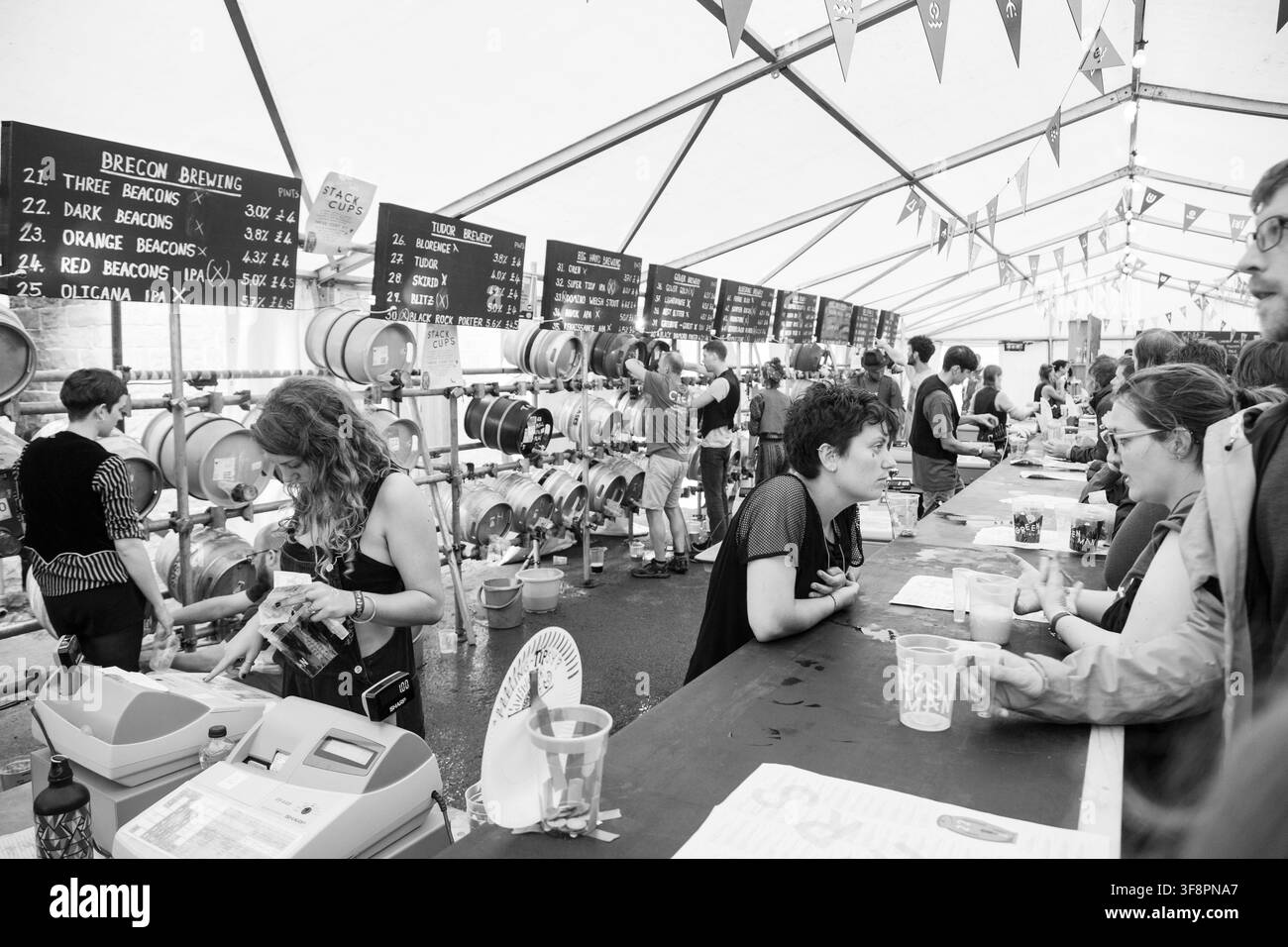 TENDONE DELLA BIRRA AL FESTIVAL AFFOLATO IN BIANCO E NERO, REPORTAGE, FESTIVAL GREEN MAN 2016, BRECON, GALLES, REGNO UNITO, 2016: In un tendone del festival strapieno, il personale serve bevande da una lunga fila di botti di birra mentre i clienti aspettano lungo il bancone affollato del bar. Foto: Rob Watkins. INFO: Il Festival Green Man è iniziato nel 2003 in Galles. Si tiene ogni anno nel terzo fine settimana di agosto nelle Brecon Beacons e celebra musica alternativa, arte, letteratura, scienza e cultura a misura di famiglia in uno splendido scenario montano. Foto Stock