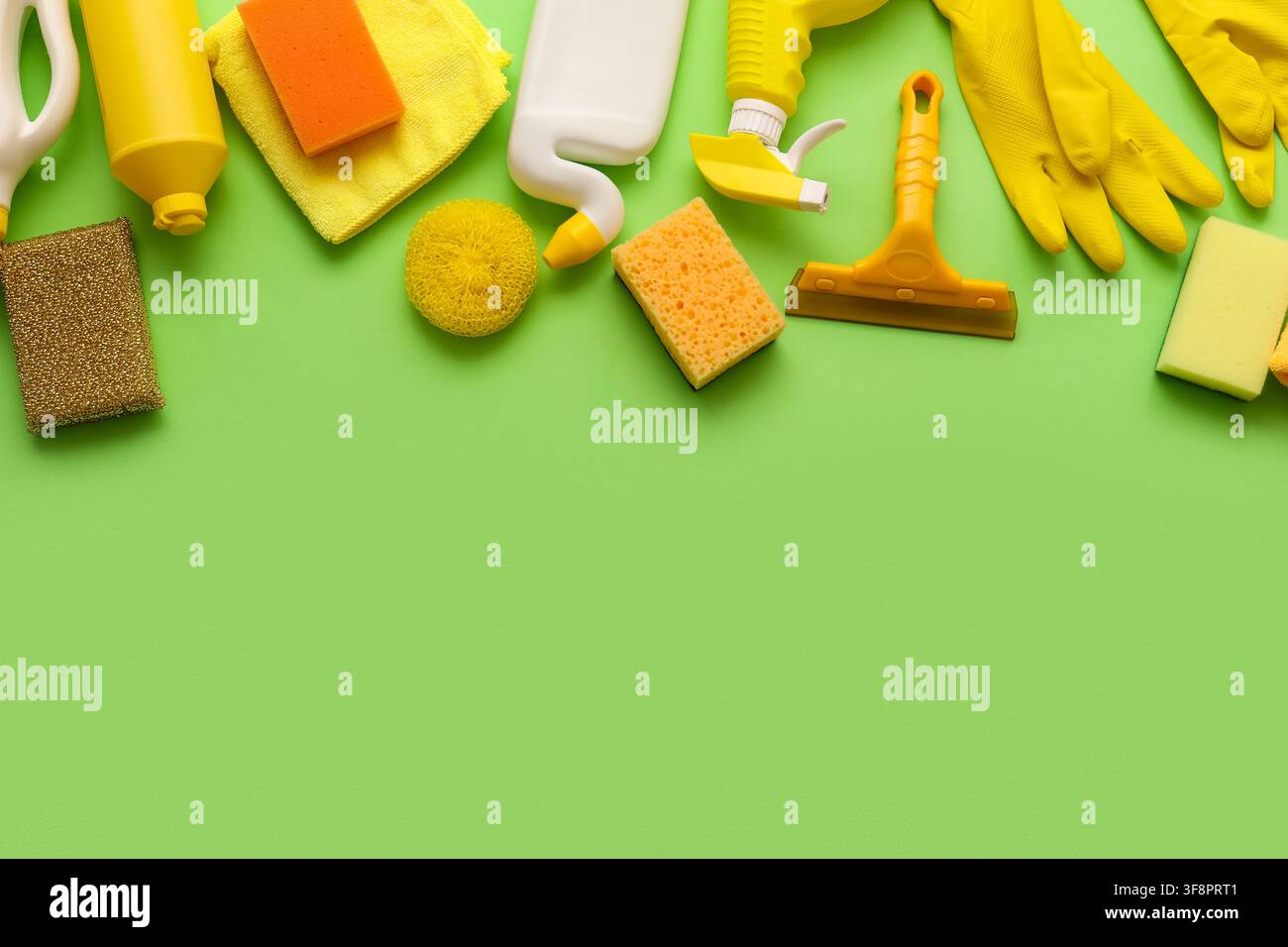 Assortimento di prodotti e articoli per la pulizia gialli e arancioni disposti su uno sfondo verde brillante con spazio libero Foto Stock