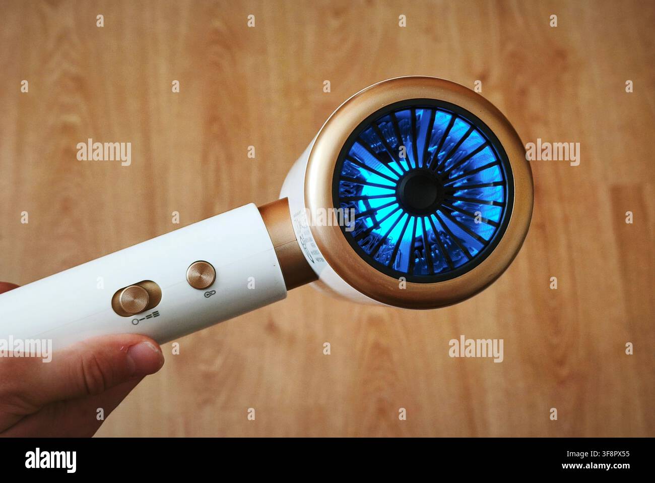 Asciugacapelli moderno ad alta velocità con tecnologia ionica a luce LED blu e design dorato tenuto in mano - Immagine stock catturata con smartphone