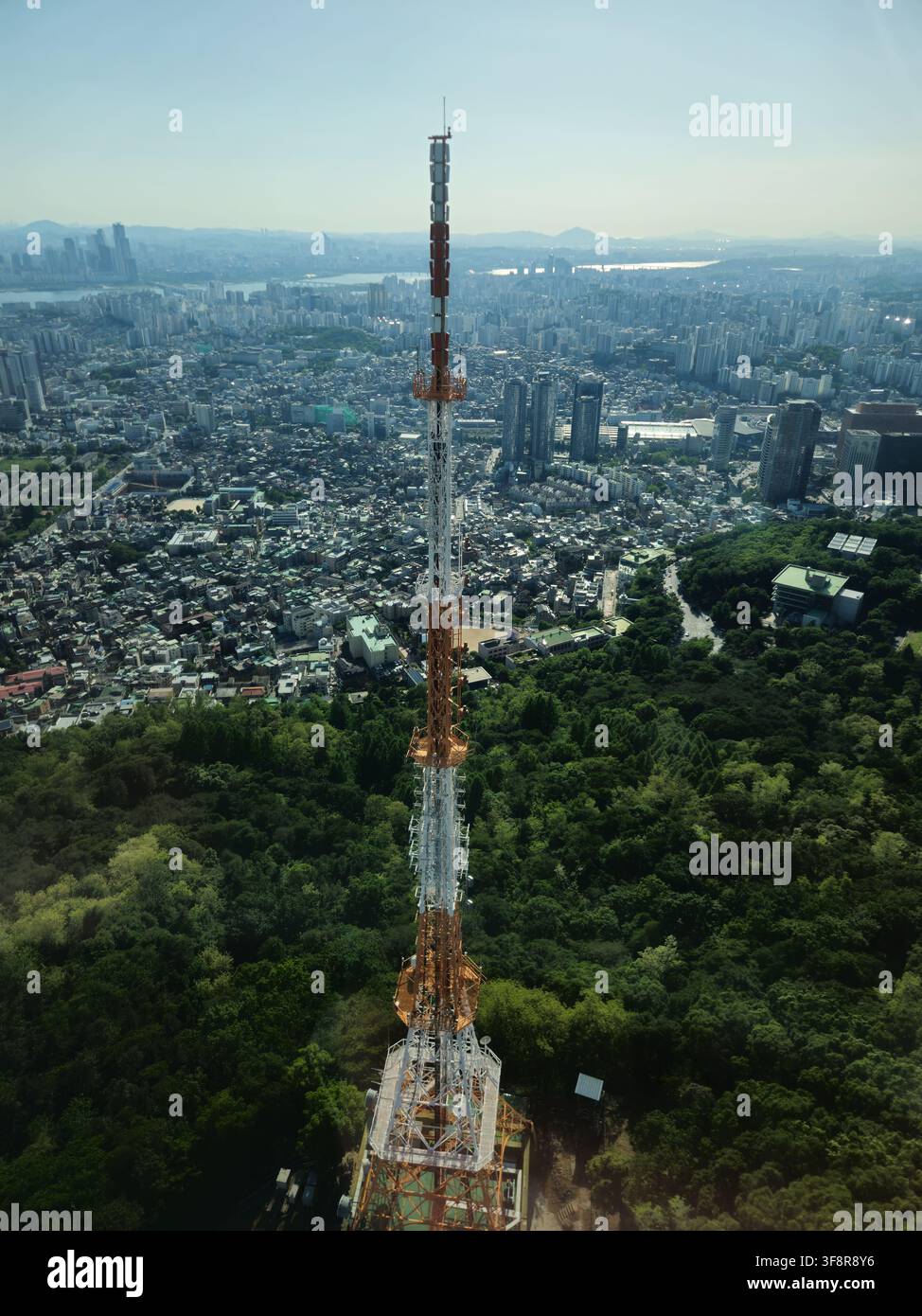 Vista aerea di una torre di comunicazione sopra una città densa e colline boschive Foto Stock