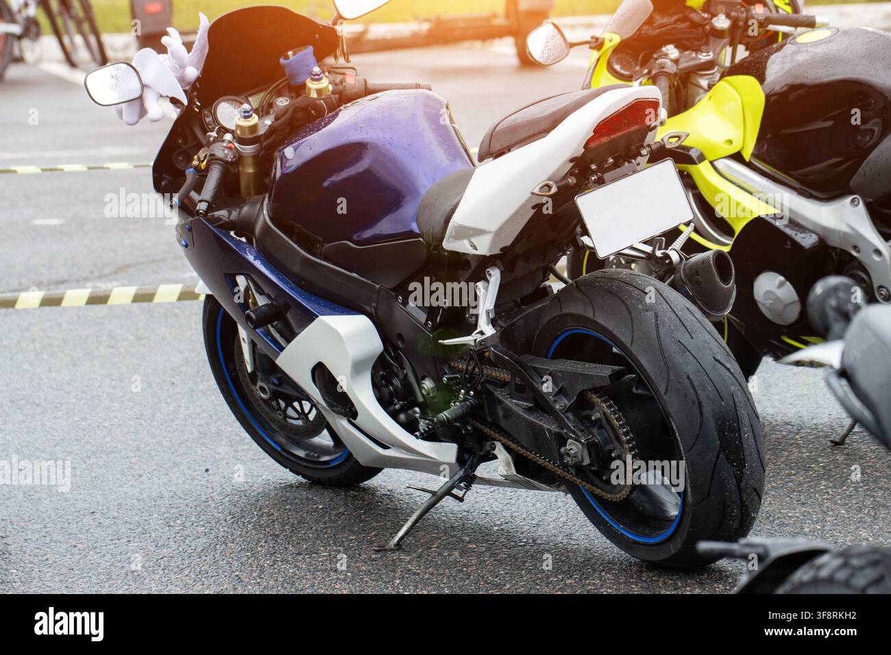 Moto sportiva con carrozzeria blu e bianca parcheggiata su asfalto bagnato, gocce d'acqua visibili sul serbatoio e sul sedile, luce intensa dell'ora dorata Foto Stock