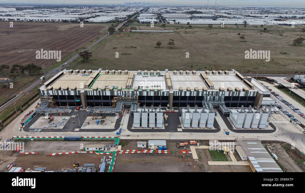 Grande struttura di data center in costruzione con unità di raffreddamento e parcheggio, circondata da area industriale e terreni agricoli Foto Stock