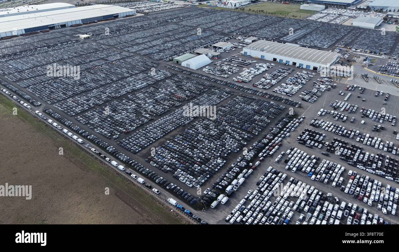 Grande struttura di stoccaggio con migliaia di veicoli nuovi in attesa di spedizione, che mostra la produzione di massa Foto Stock