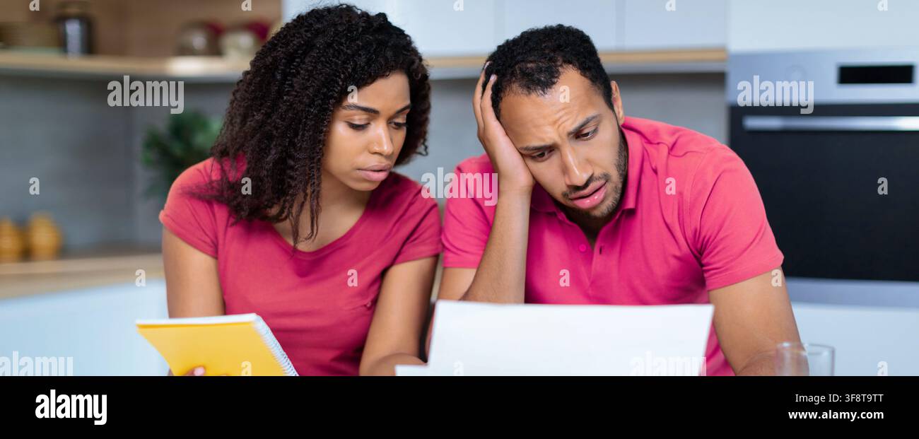 Uomo e donna neri preoccupati che guardano documenti finanziari in cucina, situazione stressante Foto Stock