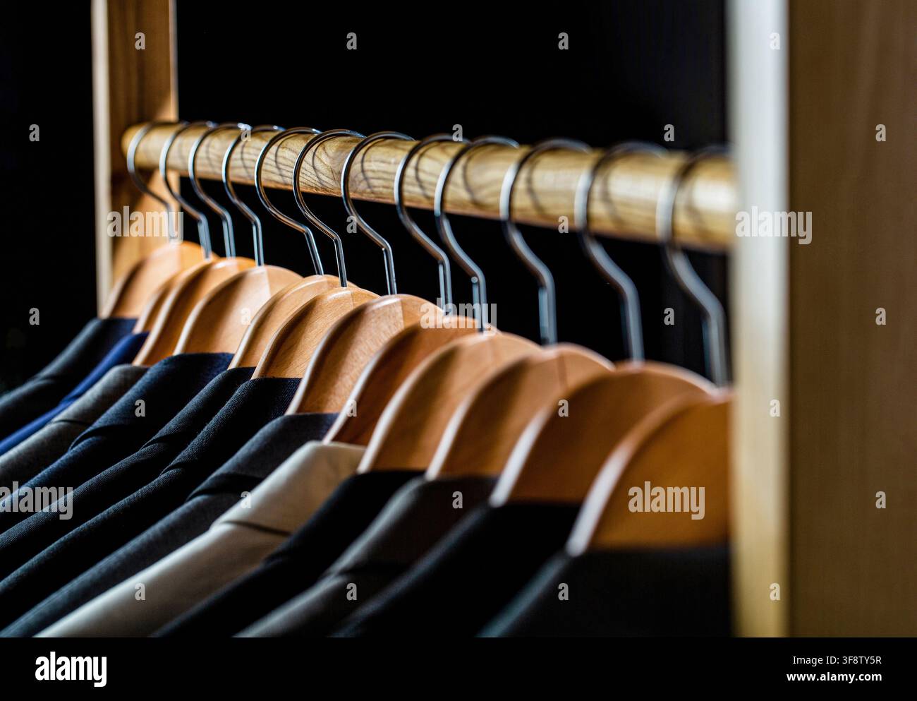 Abiti da uomo in diversi colori appesi su appendiabiti in un negozio di abbigliamento al dettaglio, primo piano. Camicie da uomo, completo appeso su scaffale. Appendiabiti con giacche sopra Foto Stock