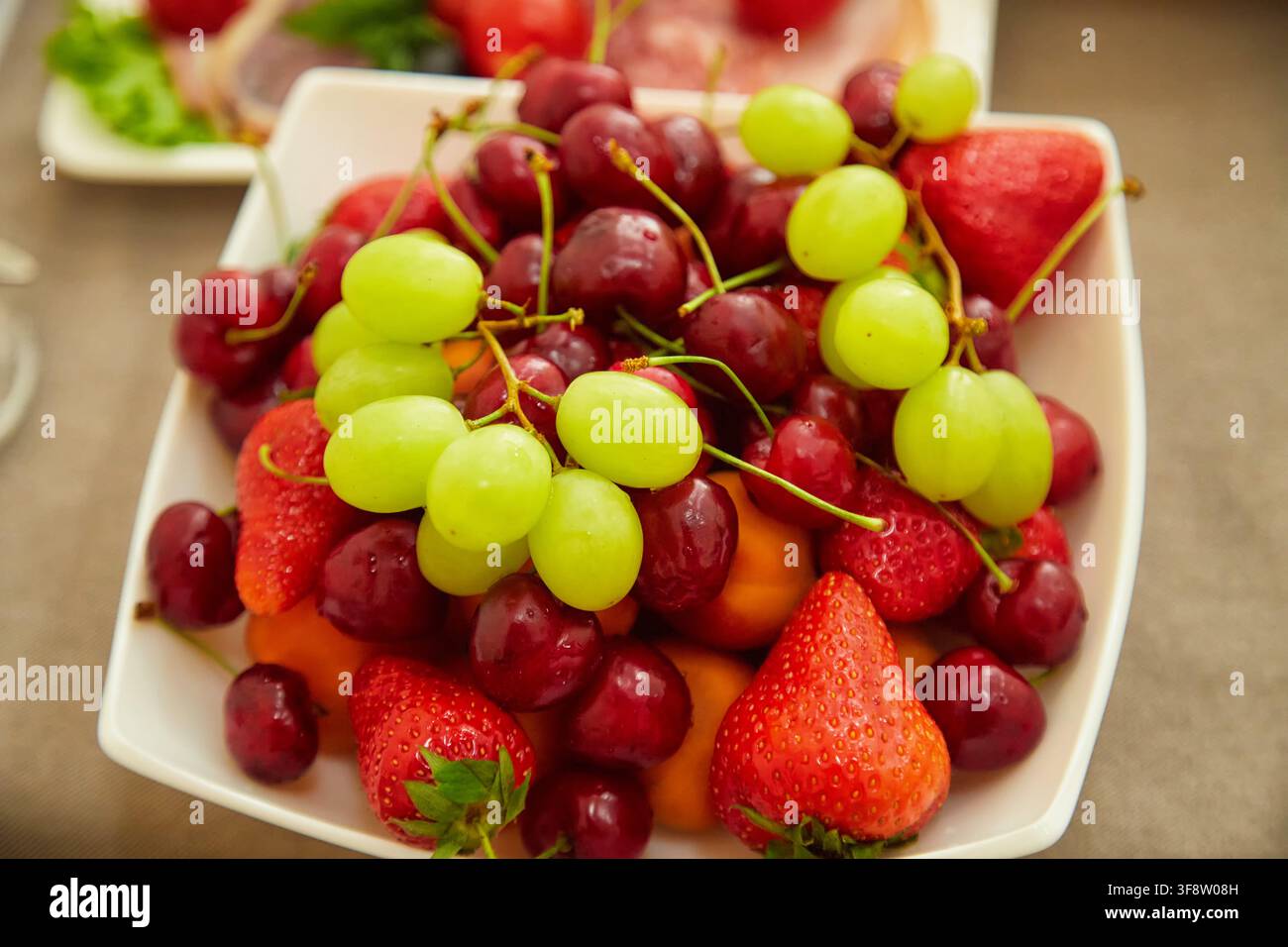 Piatto colorato di fragole fresche, ciliegie dolci e uva verde. Cibo sano, frutta estiva, dessert e concetto di tavola festosa. Foto Stock
