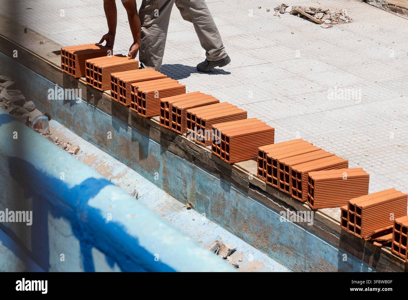 Muratore che sistema mattoni cavi in argilla in fila per la costruzione di un muro in un cantiere Foto Stock