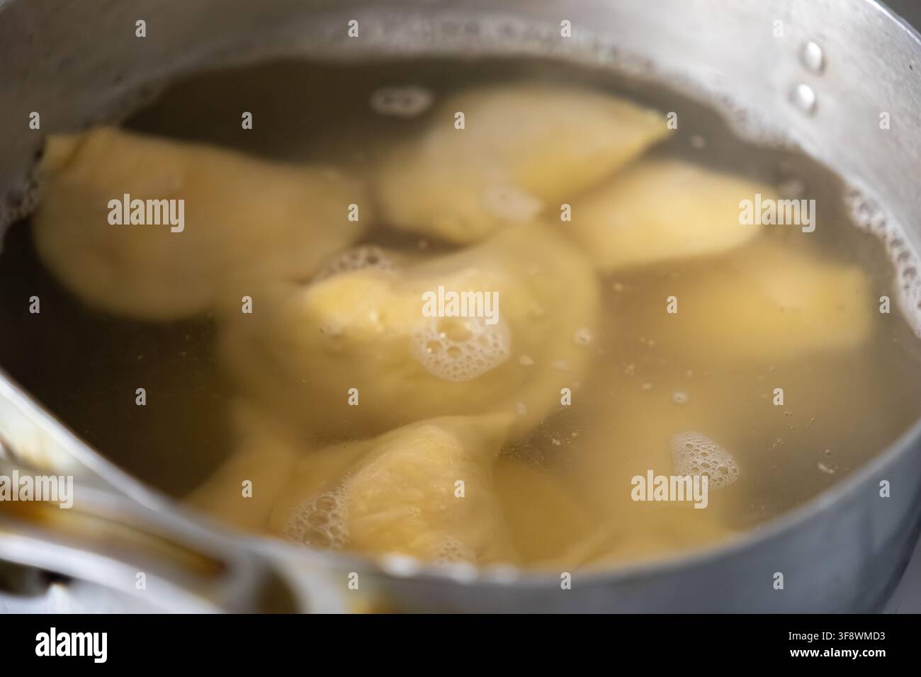 Le porzioni di impasto cuociono in una pentola scintillante di liquido ribollente, mostrando la tecnica culinaria essenziale dell'ebollizione per creare un piatto confortante per un r Foto Stock
