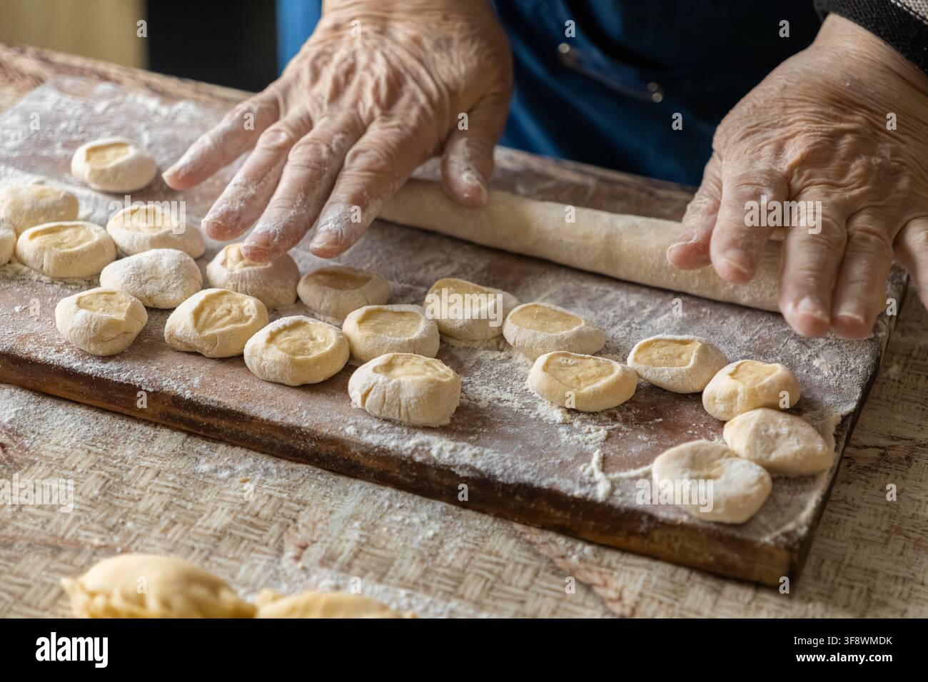Una persona anziana preme porzioni di impasto crudo su una superficie infarinata per assemblare gnocchi salati, illustrando la passione domestica e l'arte della preparazione Foto Stock