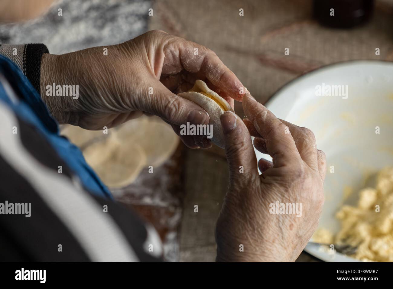 Mani mature modellano l'impasto ripieno di ripieno saporito per gli gnocchi classici, riflettendo uno stile di vita lento, pratiche di cucina autentiche e il j Foto Stock
