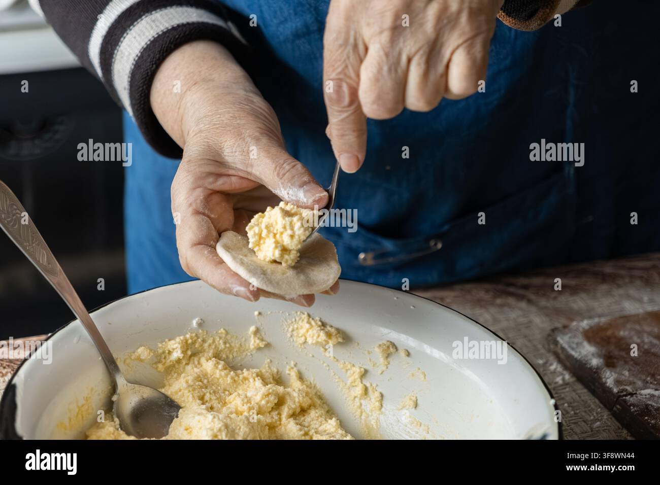 Una cuoca anziana deposita con cura un ripieno di caglio morbido su una pasta piatta usando un cucchiaio, catturando l'approccio autentico fatto a mano per la creazione di deliziosi piatti Foto Stock