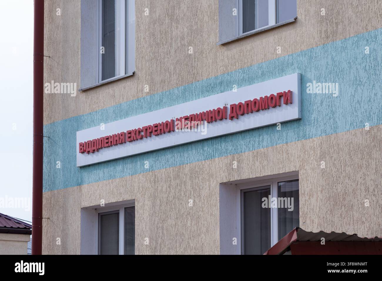 Un cartello del reparto di emergenza medico attaccato a una facciata esterna strutturata di un edificio, che fornisce indicazioni per i pazienti che necessitano di cure urgenti che arrivano a un profes Foto Stock