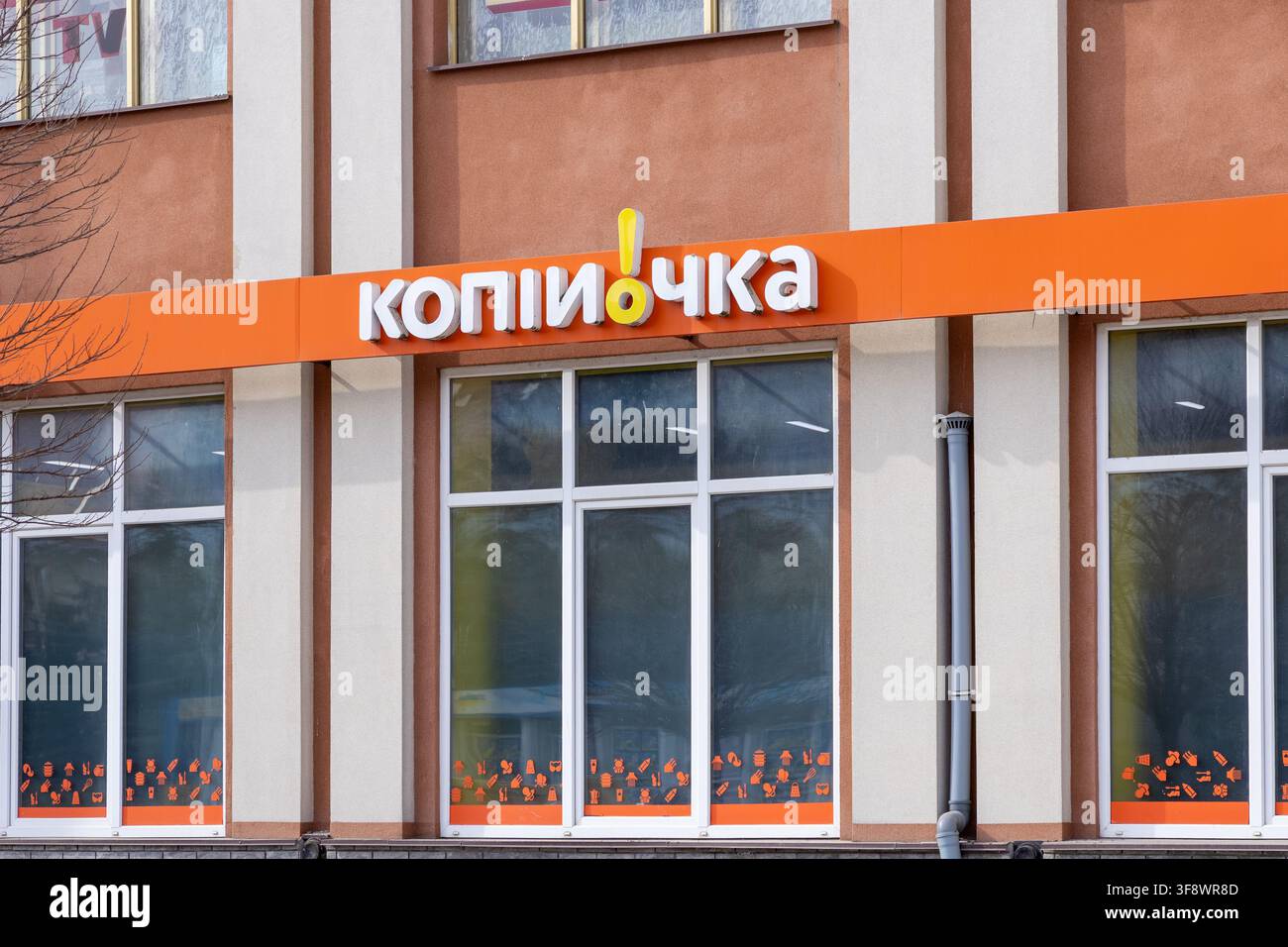 Horodok, Ucraina – 23 marzo 2026: Facciata del negozio Kopiyochka con un’insegna del logo ben visibile su una barra arancione sopra le vetrine che mostrano icone di prodotti Foto Stock