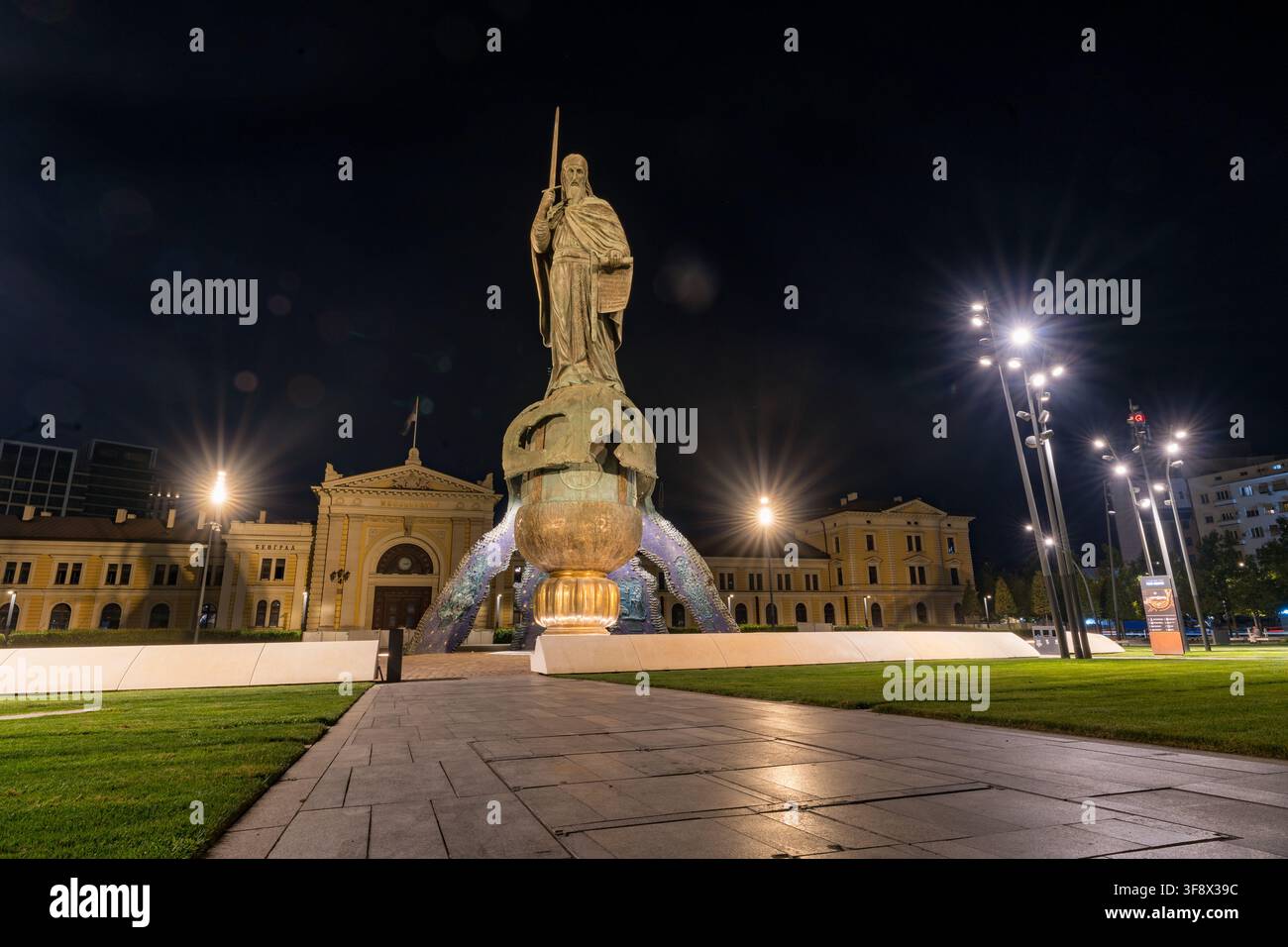 Il Monumento a Stefan Nemanja è illuminato di notte in Piazza Sava, Belgrado, Serbia, con l'antico edificio della stazione ferroviaria sullo sfondo. Bri Foto Stock