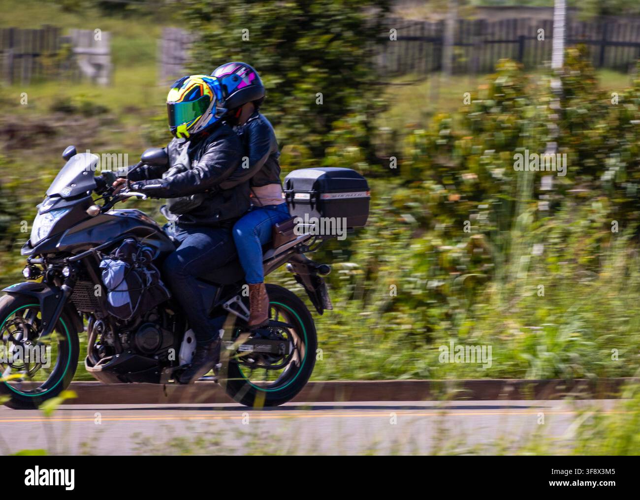 Una coppia in tour che attraversa la foresta pluviale amazzonica su una moto fuoristrada nera con la vegetazione verde sullo sfondo Foto Stock