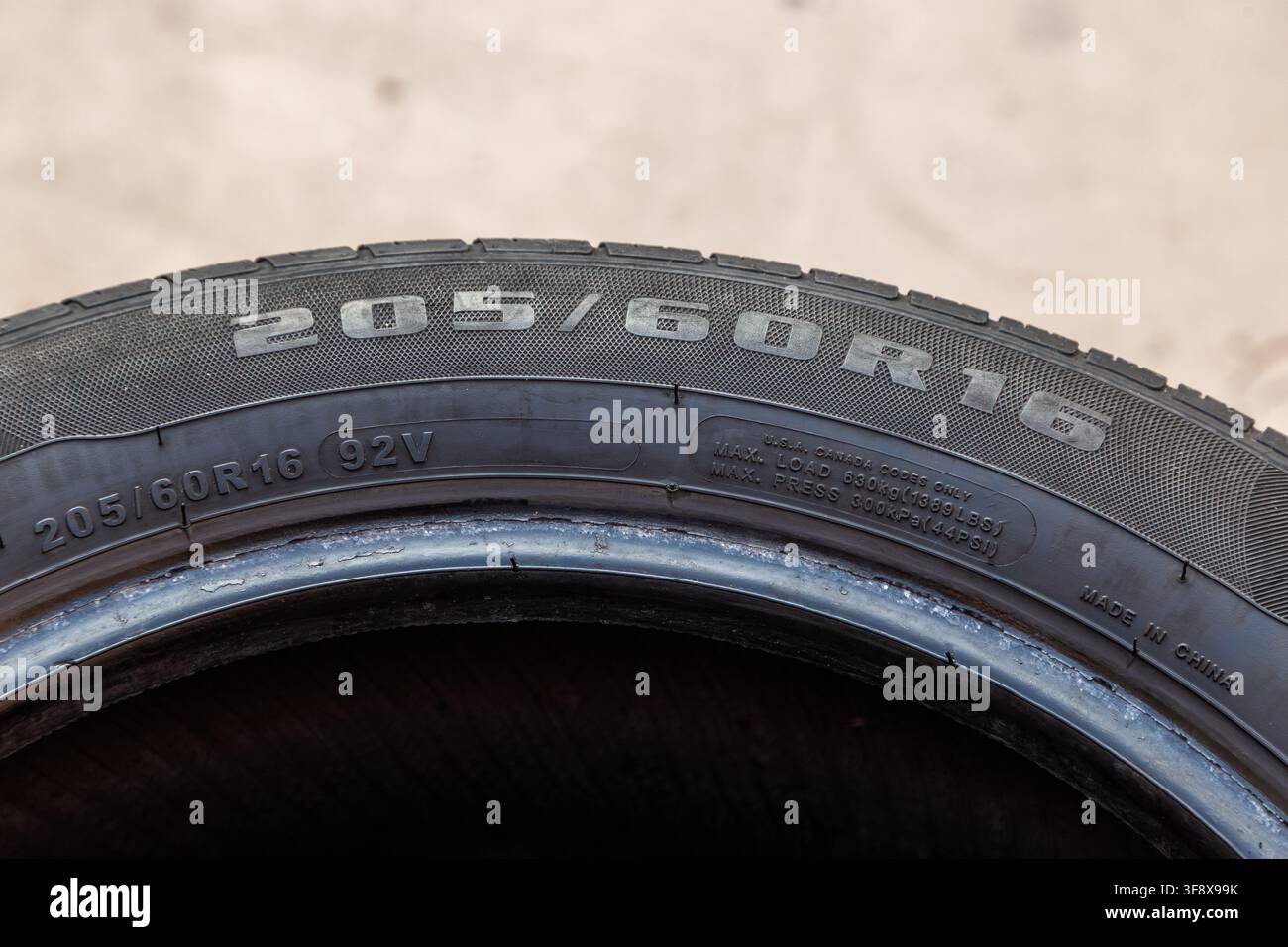 Primo piano dettagliato che cattura il testo e i numeri in rilievo sul fianco di un pneumatico per auto. Le specifiche visibili includono la dimensione del pneumatico "205 60R16", il carico massimo "92V", un Foto Stock