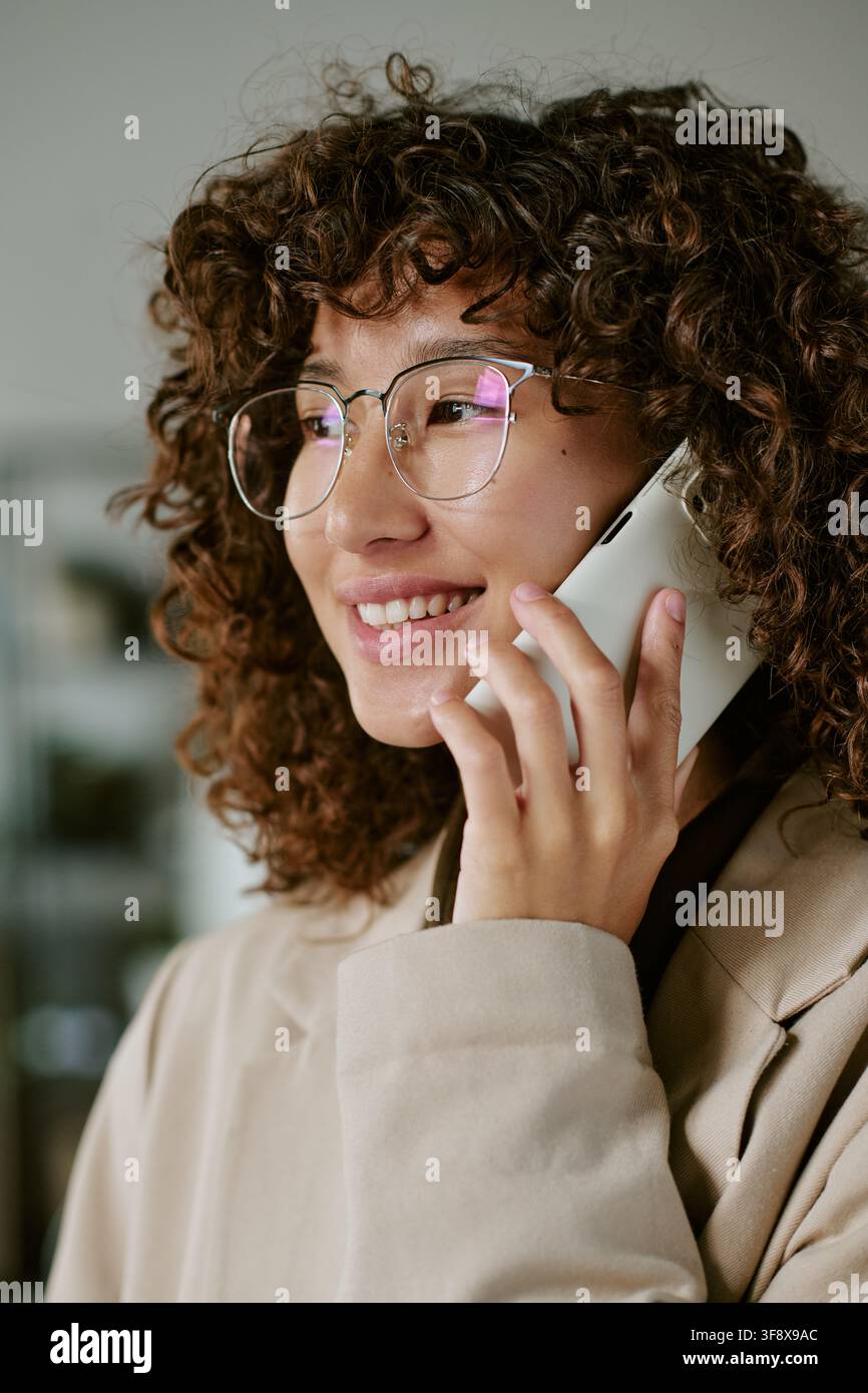 Donna d'affari biracial sorridente che parla al telefono in ufficio Foto Stock