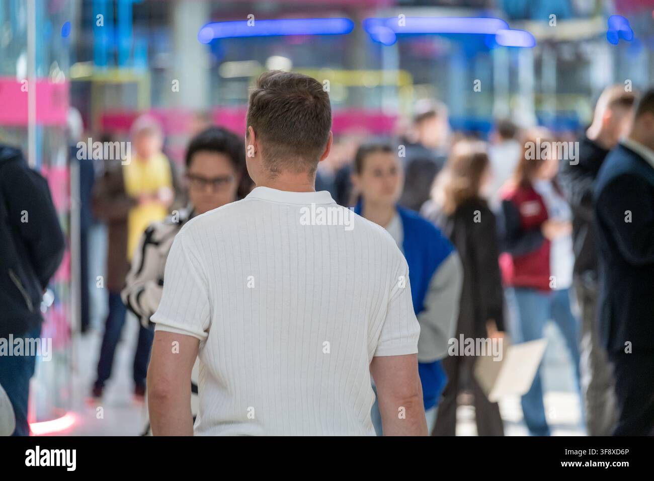 Uomo con camicia bianca si dirige verso un piano fieristico affollato con banchi colorati sullo sfondo. Foto Stock