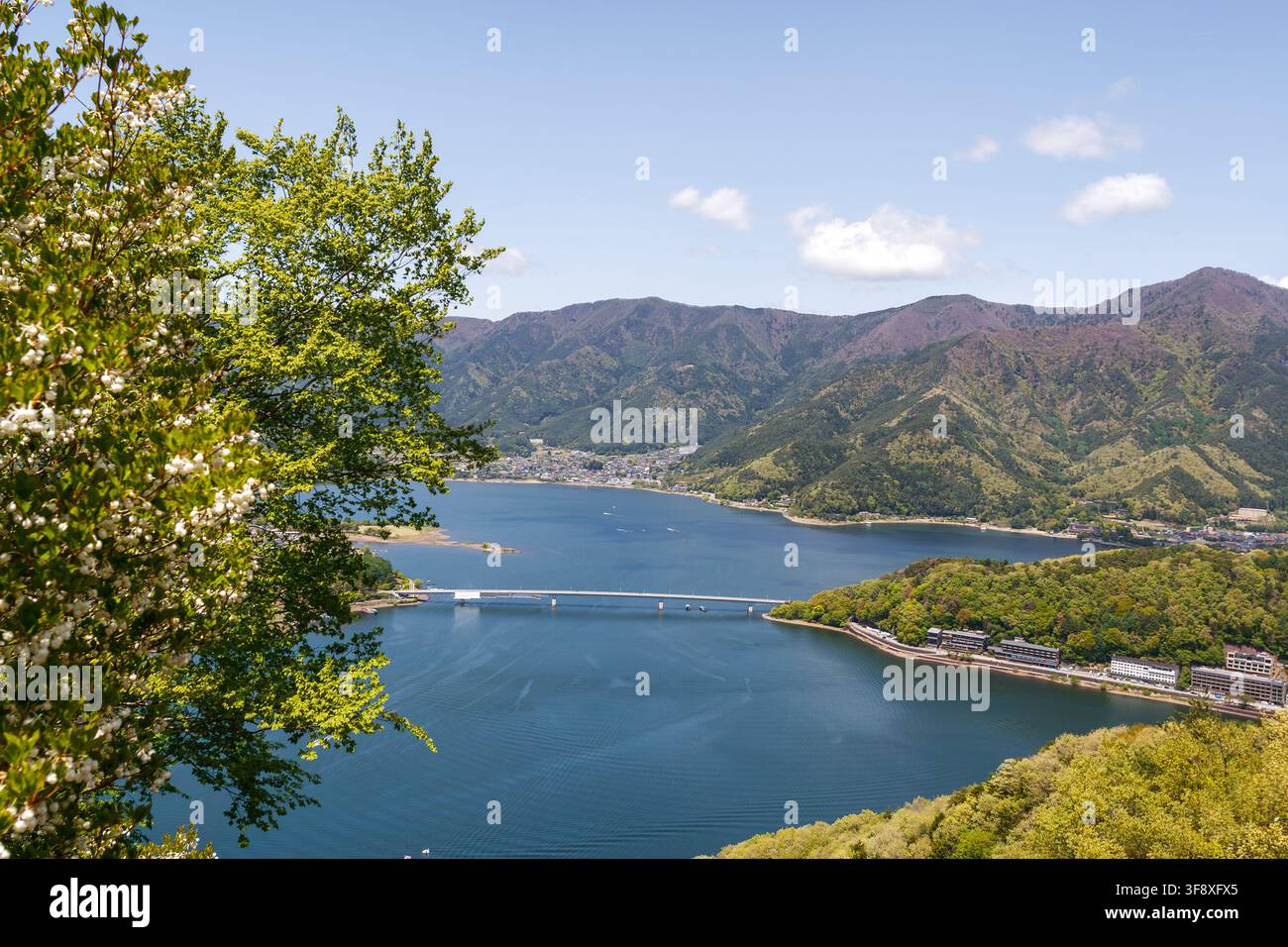 YAMANASHI, GIAPPONE - 5 LUGLIO 2025: Bella vista panoramica del lungolago di Kawaguchi con un ponte e una catena montuosa sotto un cielo azzurro in estate. Foto Stock