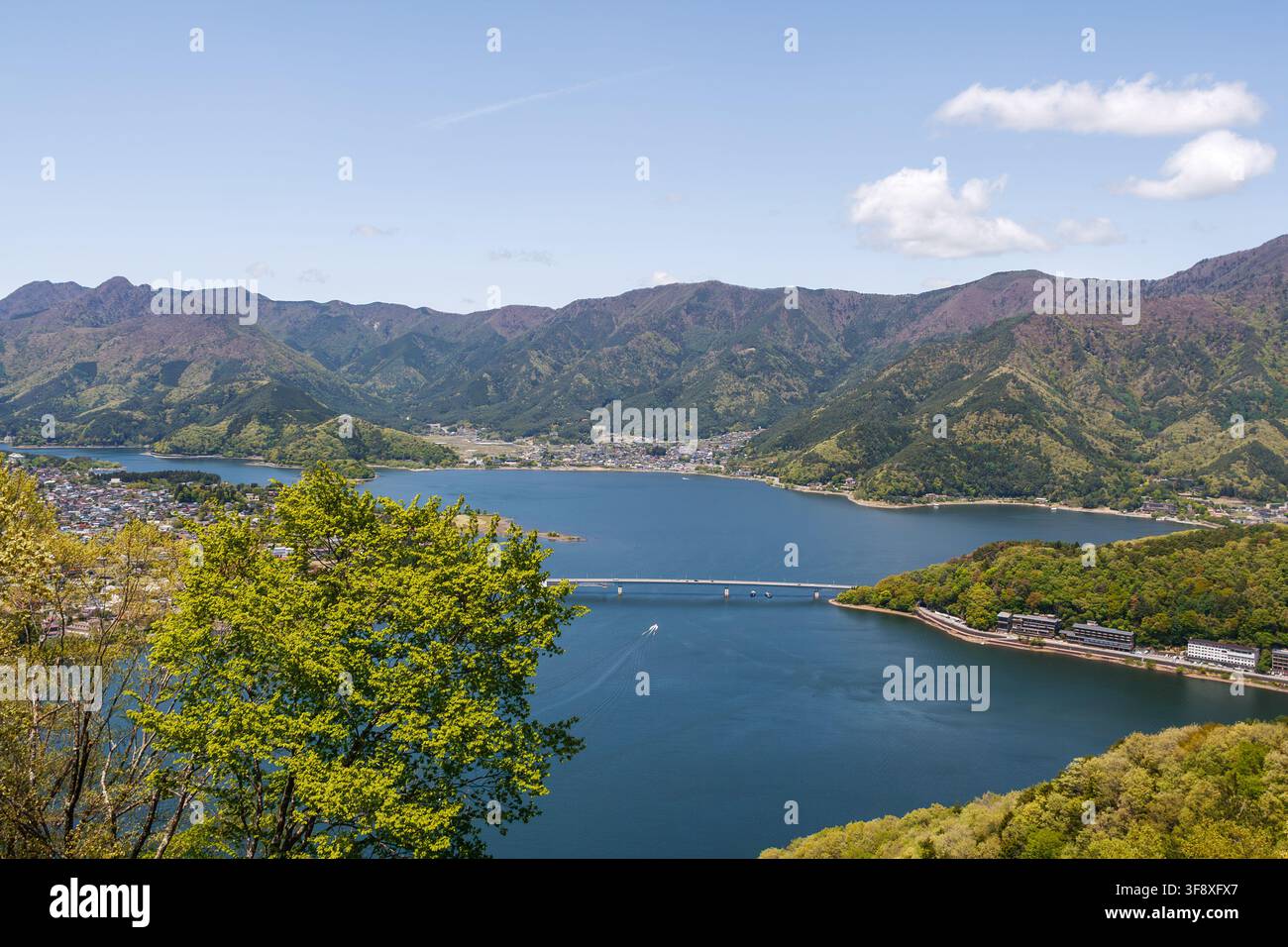 YAMANASHI, GIAPPONE - 5 LUGLIO 2025: Bella vista panoramica del lungolago di Kawaguchi con un ponte e una catena montuosa sotto un cielo azzurro in estate. Foto Stock