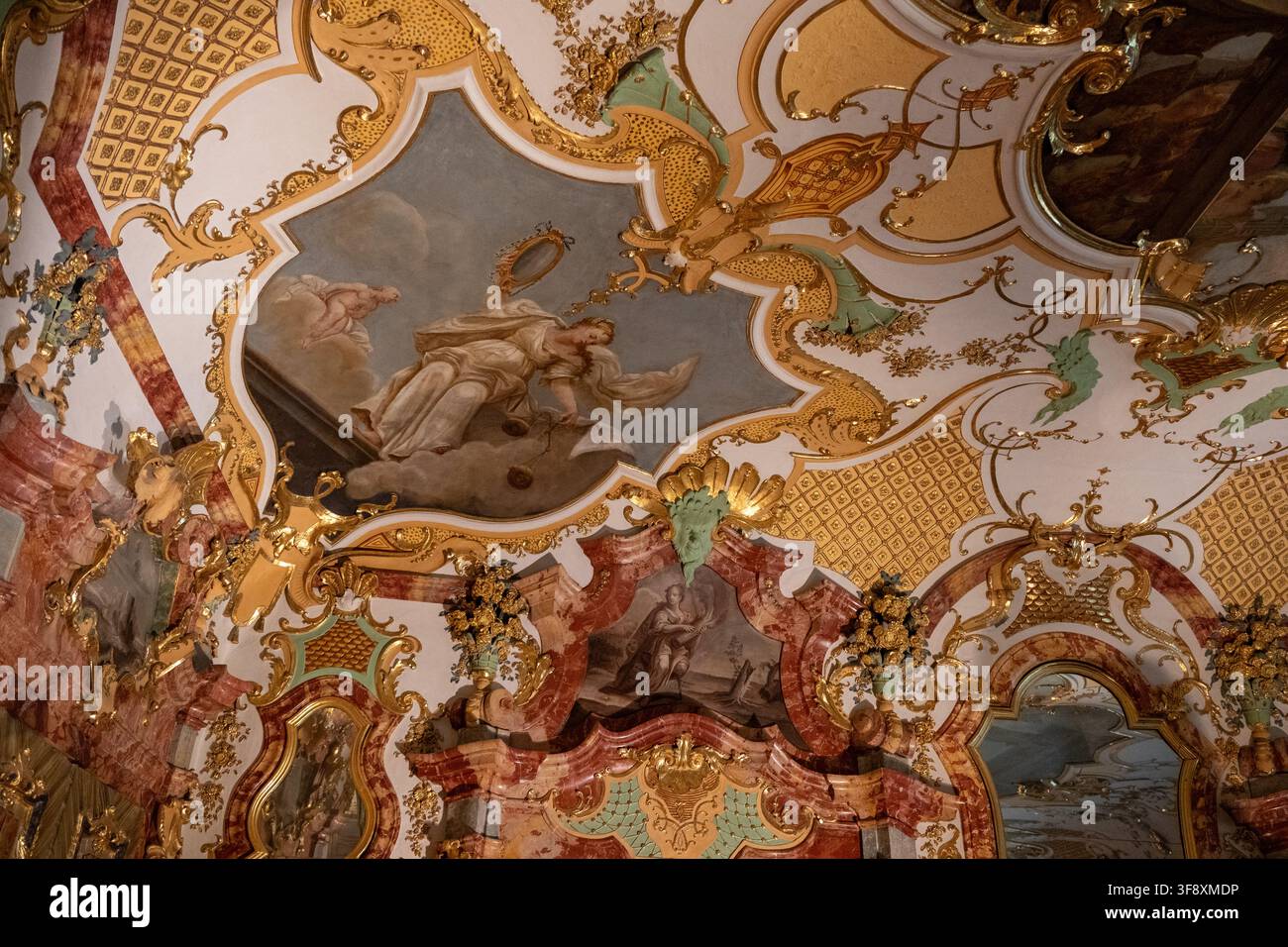 Kempten, Germania - 26 lug 25: Vista ravvicinata di un medaglione religioso rococò dorato con cherubini e drappeggi rossi all'interno della Residenza di Kempten in Bavaria. Foto Stock
