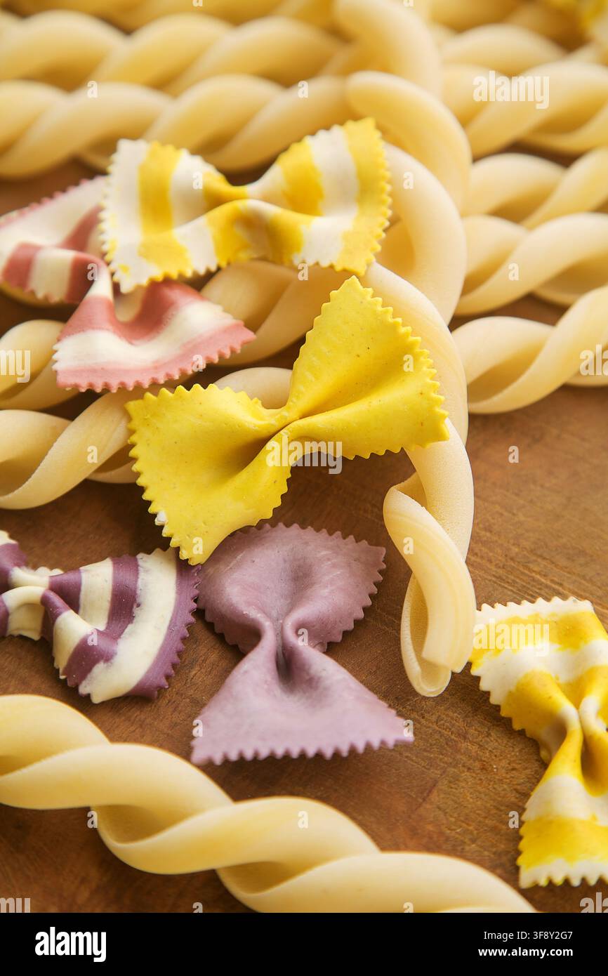 maccheroni (pasta) italiani fatti a mano multicolori secchi chiamati farfalle, primo piano in una pirofila bianca su sfondo di legno. Foto Stock