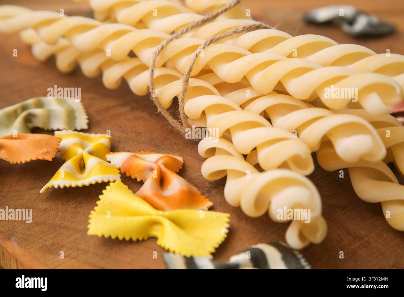 maccheroni (pasta) italiani fatti a mano multicolori secchi chiamati farfalle, primo piano in una pirofila bianca su sfondo di legno. Foto Stock