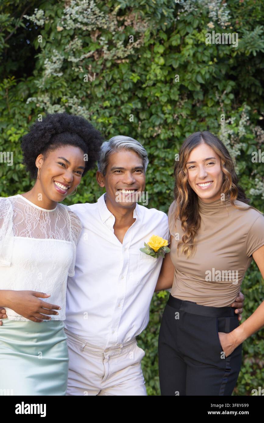 Tre amici in piedi e sorridenti in giardino indossano un top di pizzo bianco, bottone rosa giallo Foto Stock