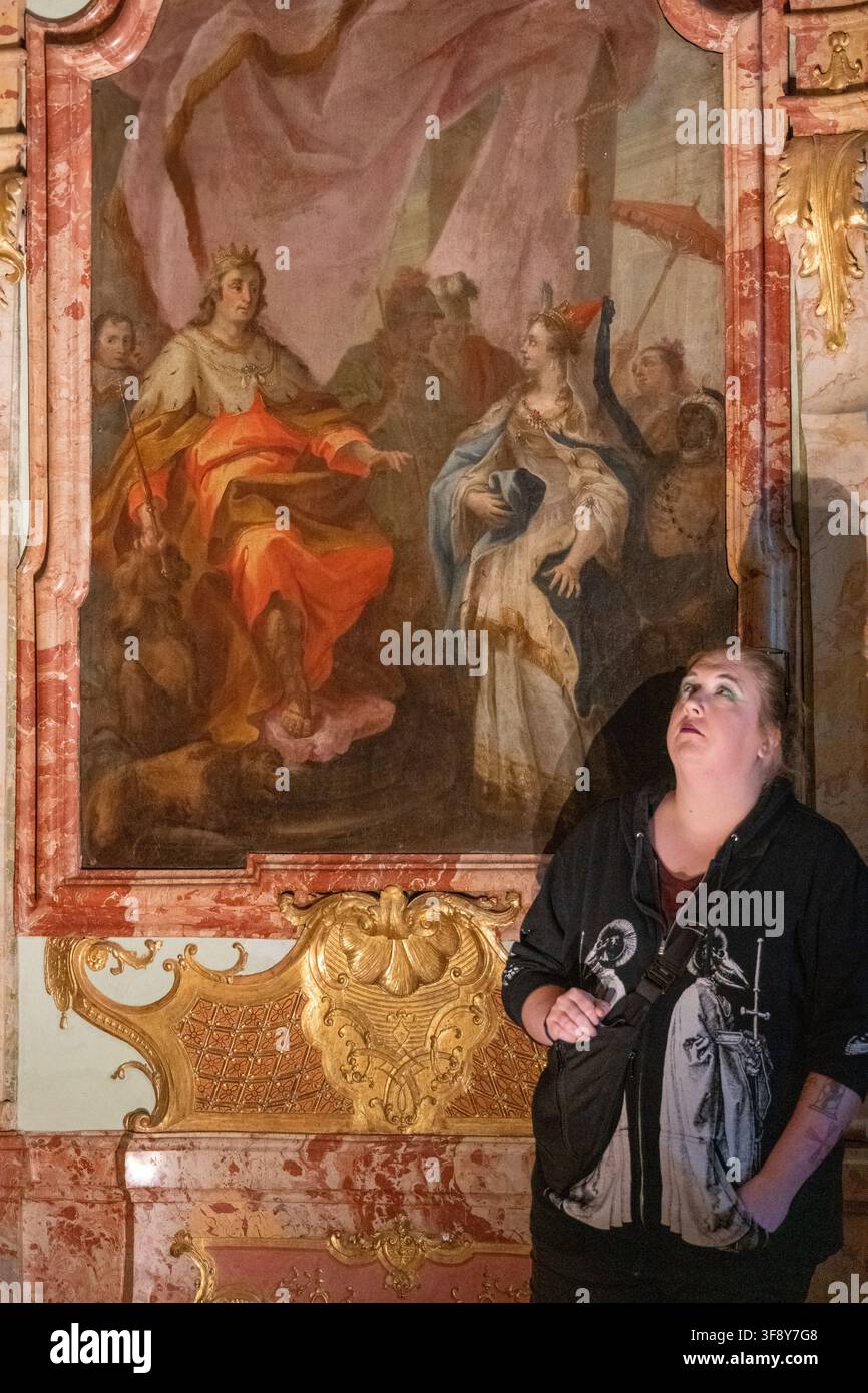 Un visitatore adulto si trova accanto a un grande affresco e a una decorazione murale rococò dorata all'interno della Residenza di Kempten, in Baviera, Germania. Foto Stock
