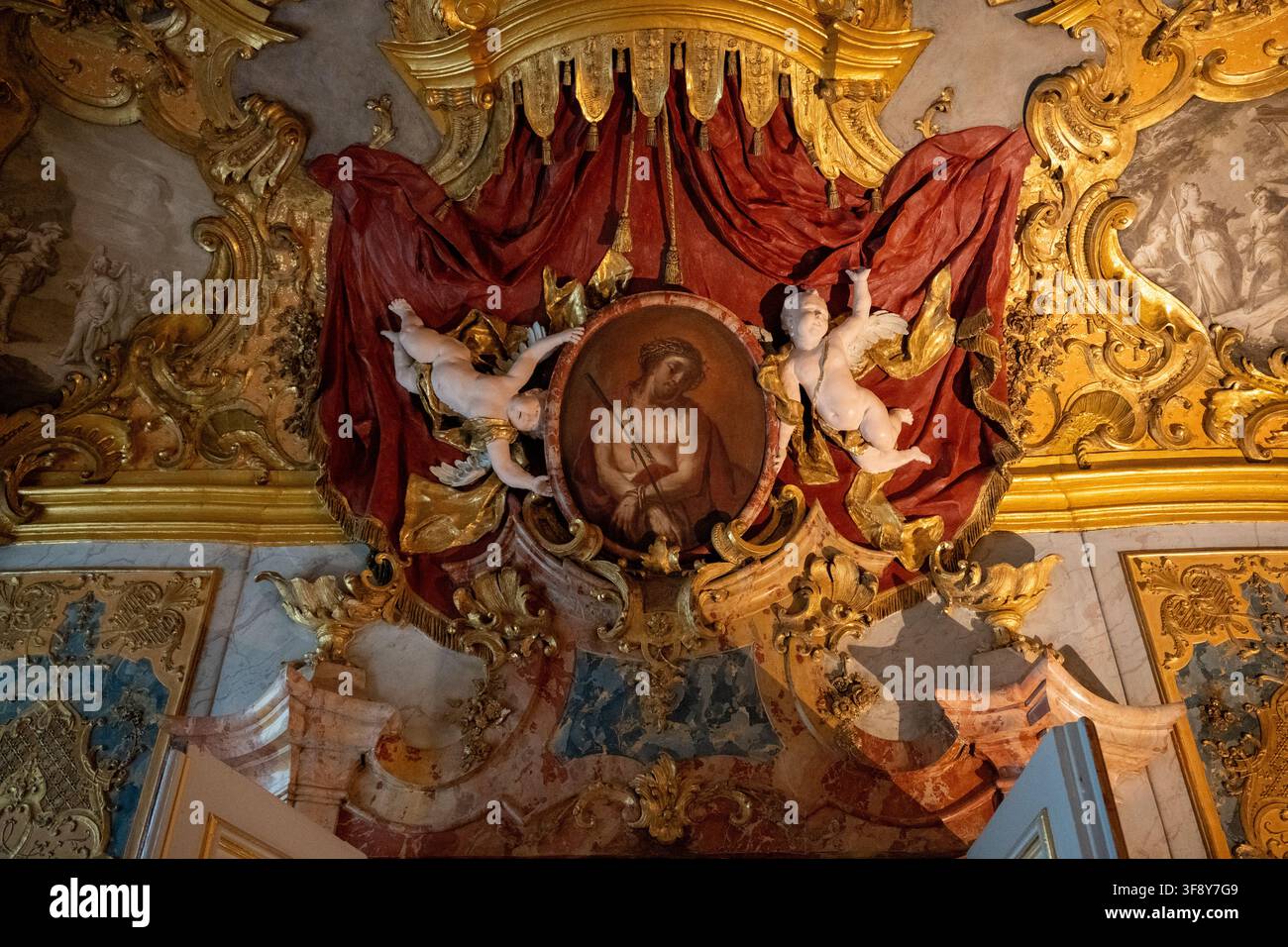 Kempten, Germania - 26 lug 25: Dettaglio di parete e soffitto rococò con stucchi dorati, cherubini, drappo rosso e medaglione religioso a Kempten, Bavaria, Foto Stock