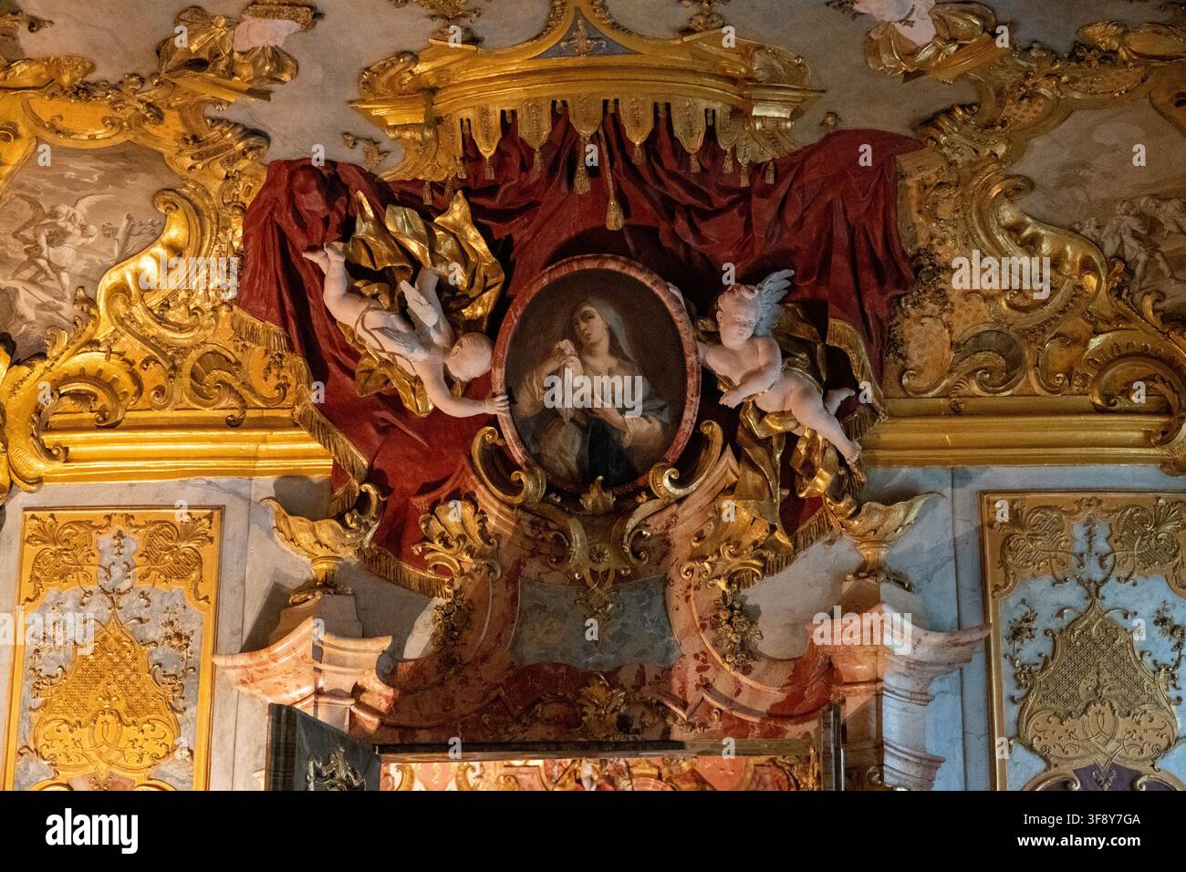 Kempten, Germania - 26 lug 25: Dettaglio dell’altare rococò dorato con cherubini, drappi rossi e pittura religiosa all’interno della Residenza di Kempten, Baviera, Ge Foto Stock