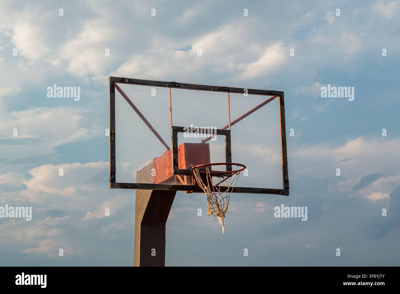 Canestro da basket all'aperto consumato con rete strappata sotto un cielo nuvoloso Foto Stock
