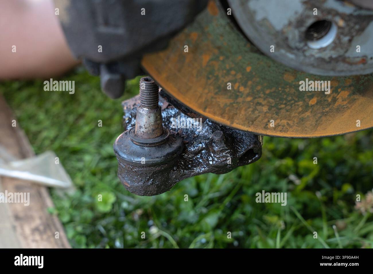 Primo piano estremo di un giunto sferico oleoso e di un disco del freno arrugginito durante la riparazione della sospensione dell'auto all'aperto Foto Stock