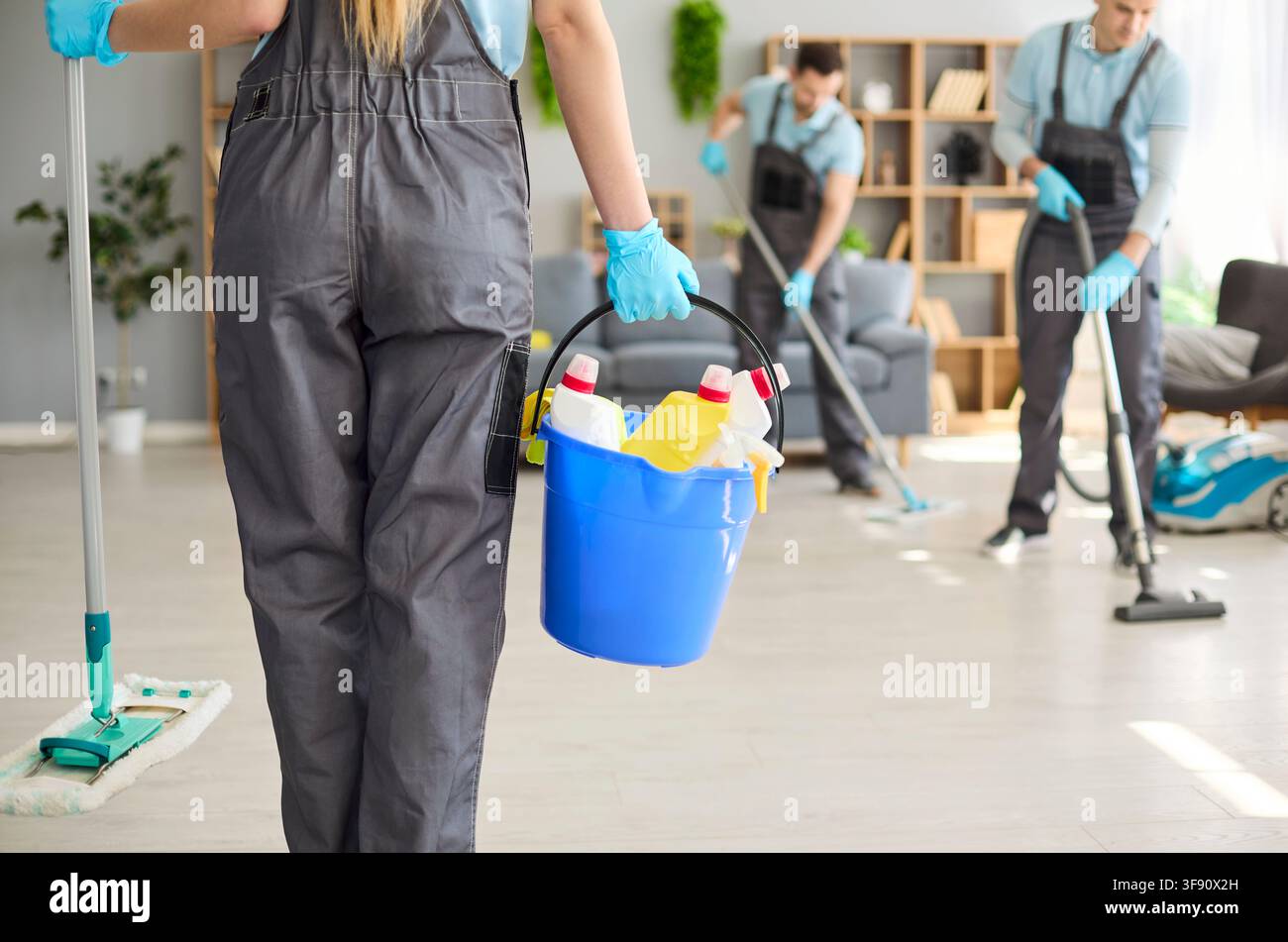 Squadra di pulizia professionale che disinfetta l'interno con secchio, guanti, mocio e aspirapolvere Foto Stock