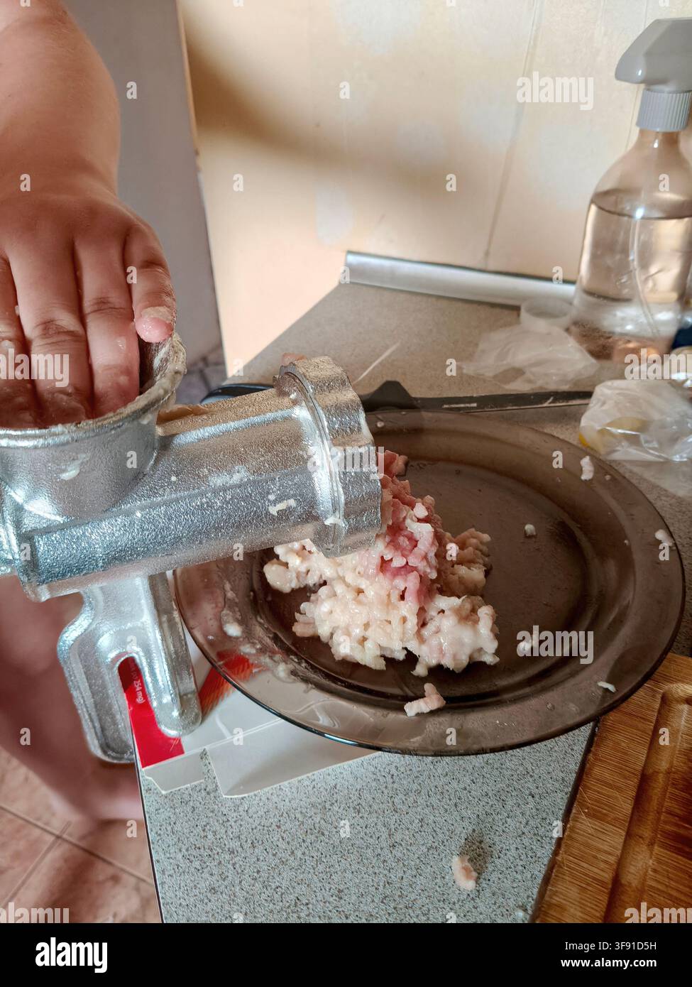 Procedimento di macinazione della carne cruda utilizzando un tritacarne meccanico manuale vintage tradizionale in cucina foto stock Foto Stock