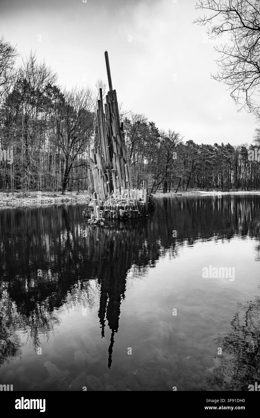L'organo di basalto si erge sopra l'acqua del lago Rakotz in Germania. Gli alberi vicini si riflettono sulla superficie dell'acqua. La scena mostra un paesaggio aspro in monocromo. Foto Stock