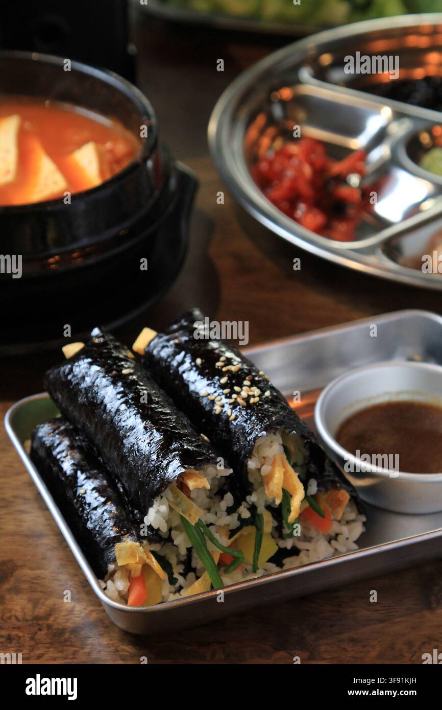 Involtini di riso con alghe coreane kimbap tagliati a pezzi serviti su un vassoio di metallo con salsa da intingere e zuppa. Foto Stock
