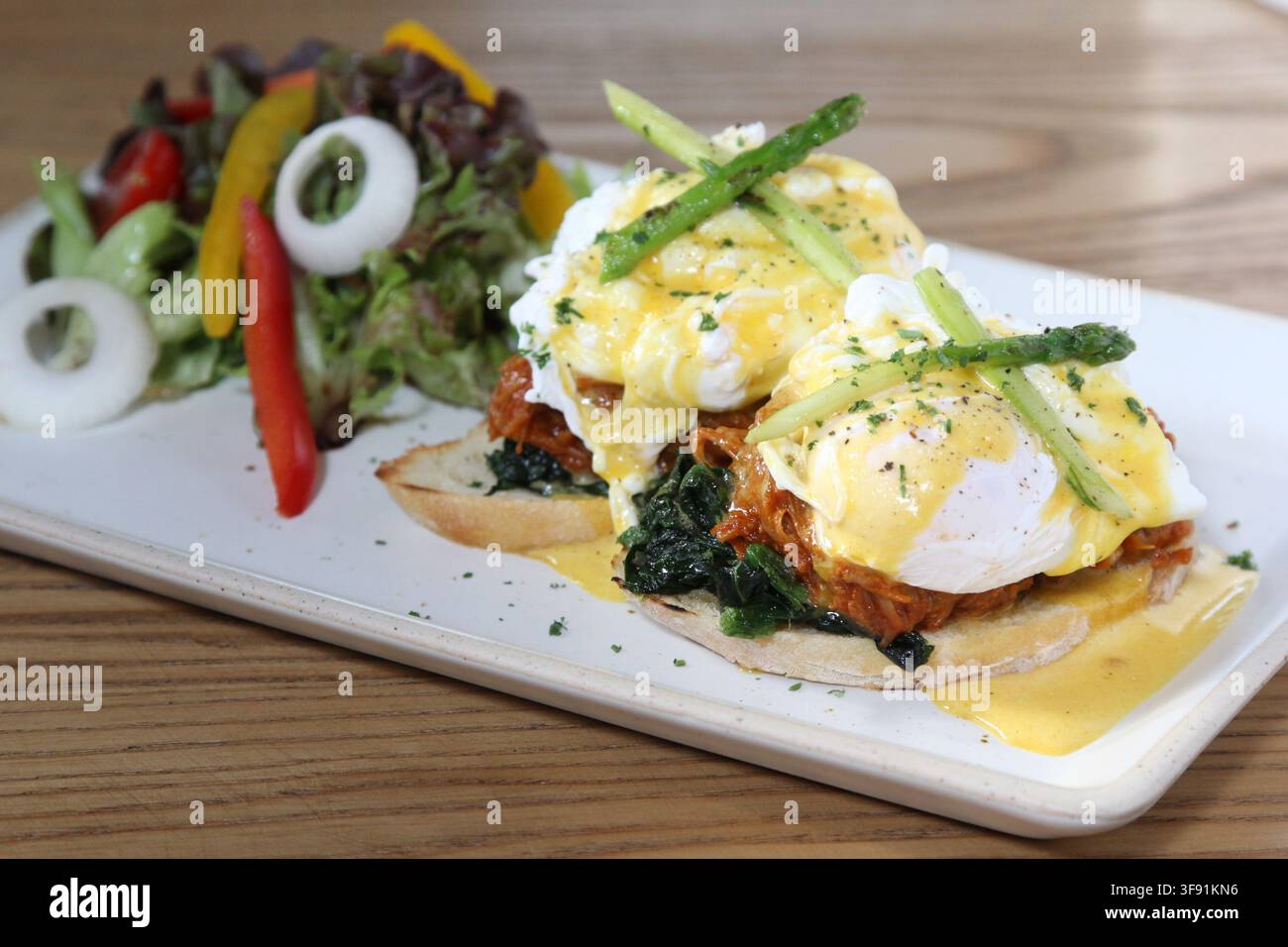 Uova Benedict con pulled pork e spinaci appassiti su muffin inglesi tostati, ricoperti di salsa olandese e asparagi, serviti con una salsa fresca a lato Foto Stock