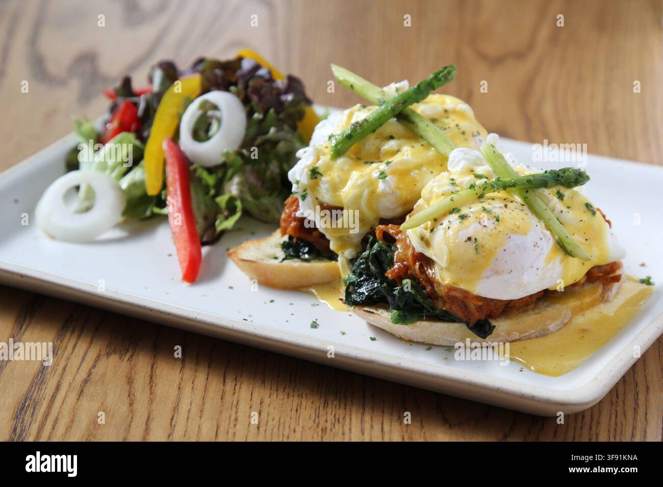 Uova Benedict con pulled pork e spinaci appassiti su muffin inglesi tostati, ricoperti di salsa olandese e asparagi, serviti con una salsa fresca a lato Foto Stock