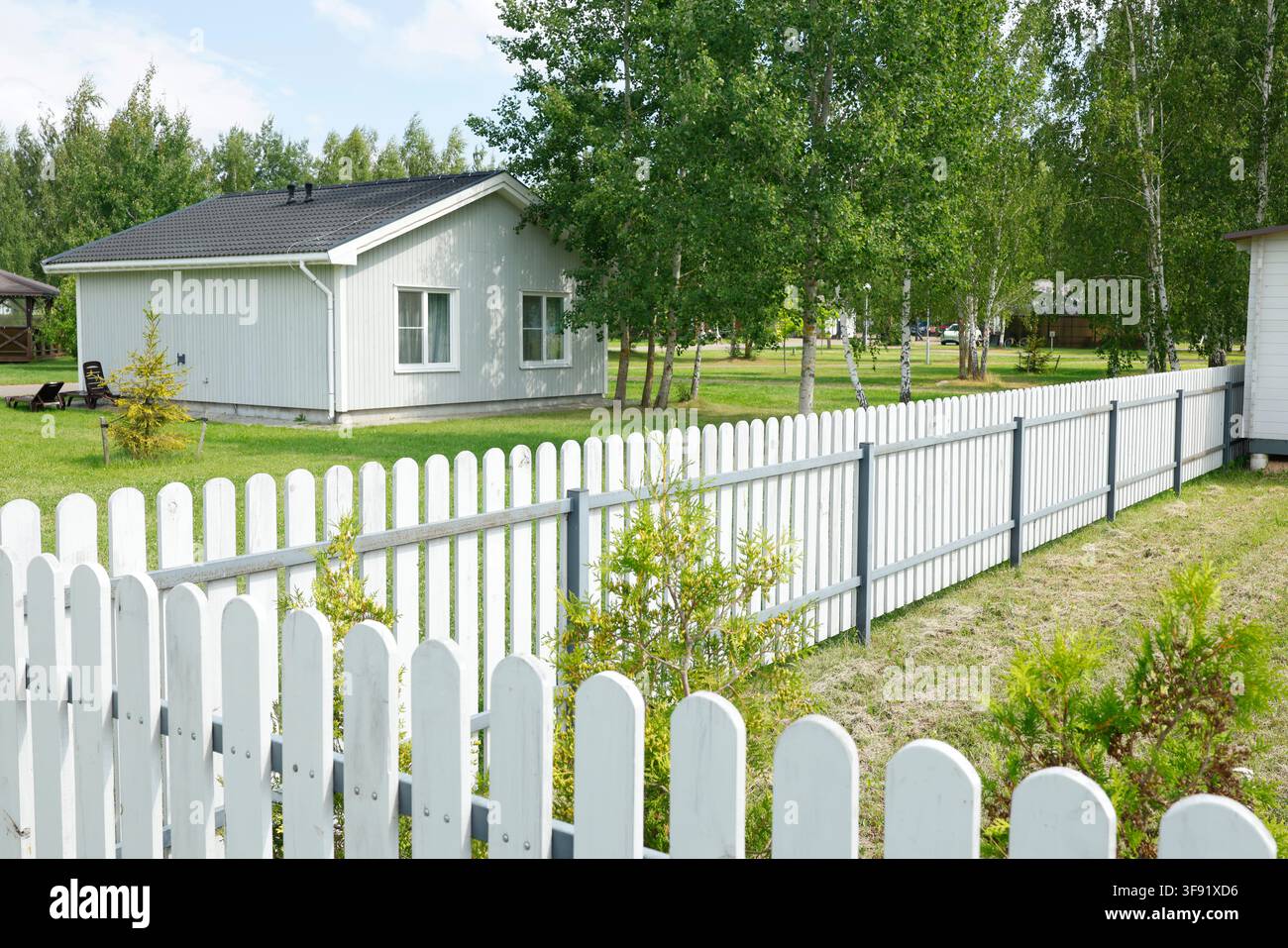 Recinzione bianca attorno a un moderno cottage di vacanza in campagna. Concetto di stile di vita all'aperto ecoturistico e lento accogliente. Famiglia in un giardino di parco tranquillo estivo Foto Stock