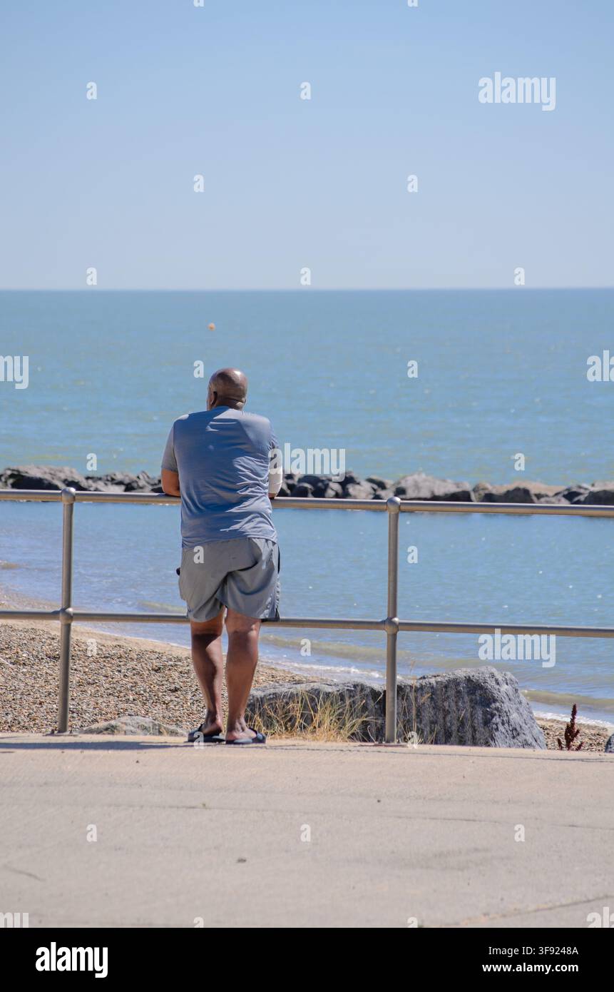 un uomo nero che guarda il mare in una calda giornata estiva nel Regno Unito Foto Stock
