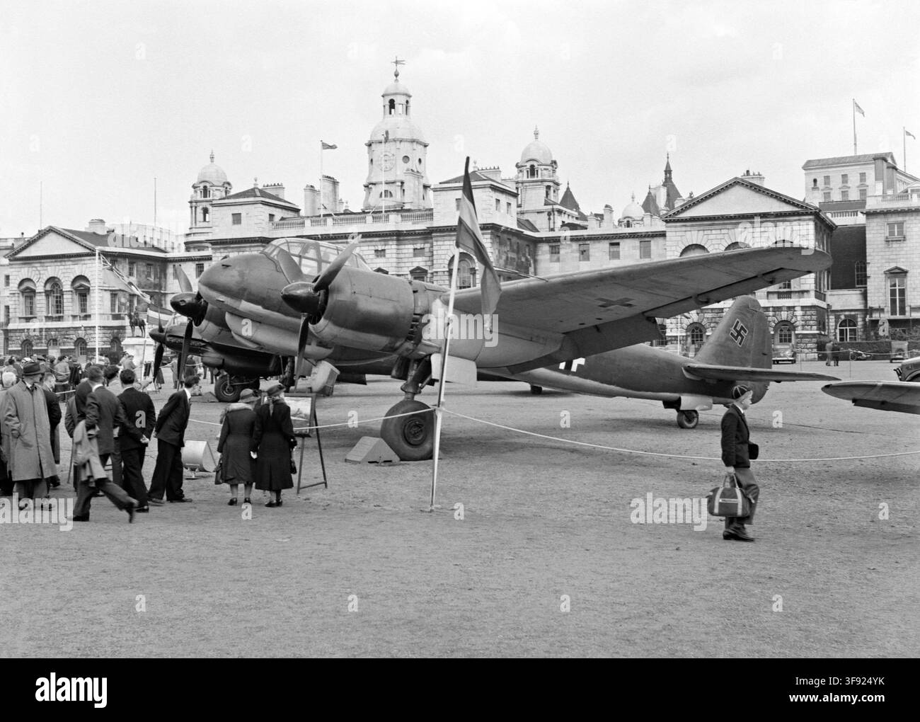 Persone che osservano un aereo tedesco catturato della Seconda Guerra Mondiale nella Horse Guards Parade, Londra, Inghilterra, Regno Unito ca. 1950. Si tratta di un aereo da combattimento multiruolo Junkers Ju88R-1. Questo aereo della Luftwaffe è stato pilotato da disertori fino alla costa scozzese il 9 maggio 1943 e, scortato da Spitfire, è atterrato alla RAF Dyce, dove è stato immediatamente circondato dalla polizia militare. L'aereo è stato numerato PJ876 dalla RAF ed è stato utilizzato per voli di indagine radio e radar. Era comune che aerei di tutte le nazionalità fossero esposti alla Horse Guards Parade, sia durante che dopo la guerra. Foto Stock