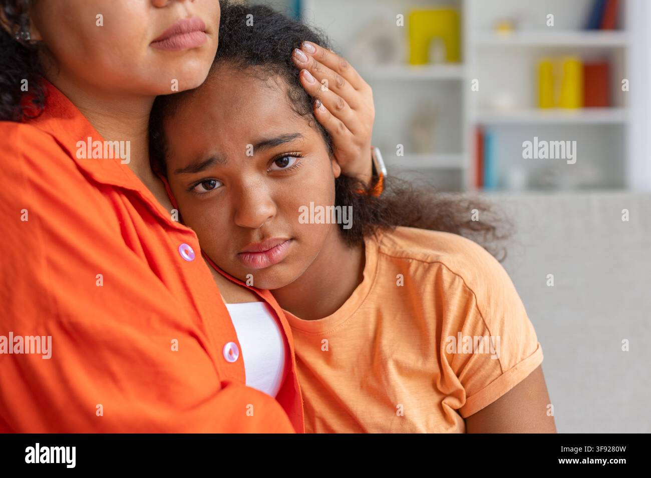 Primo piano di una figlia nera preoccupata che riposa sulla spalla della madre, guardando la telecamera Foto Stock
