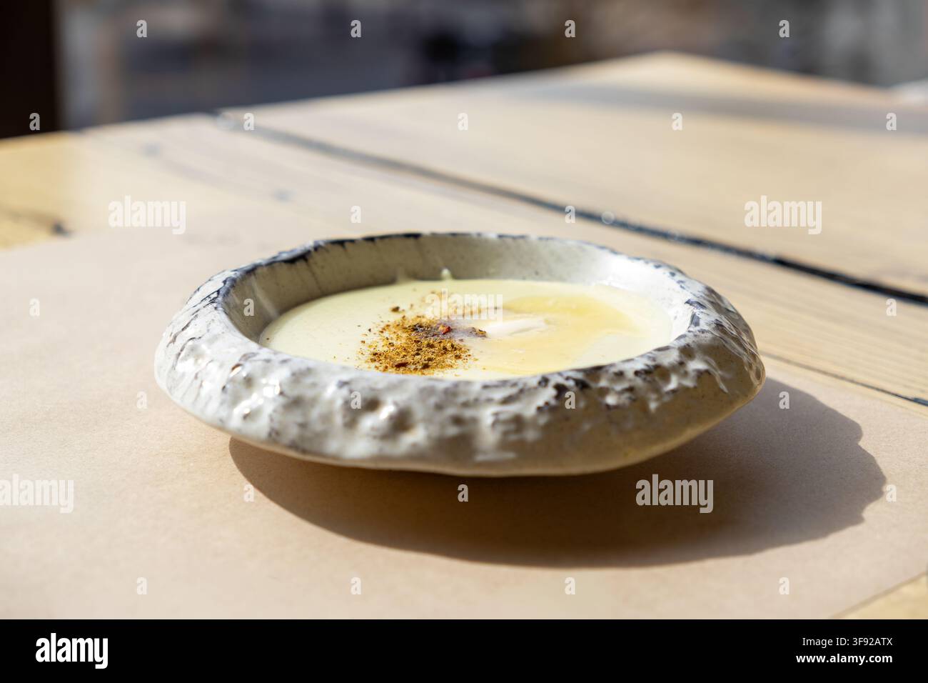 Una ciotola rustica contiene un purè di patate liscio ricoperto di formaggio fuso e condimenti saporiti, creando un'esperienza culinaria confortevole perfetta per il relax Foto Stock