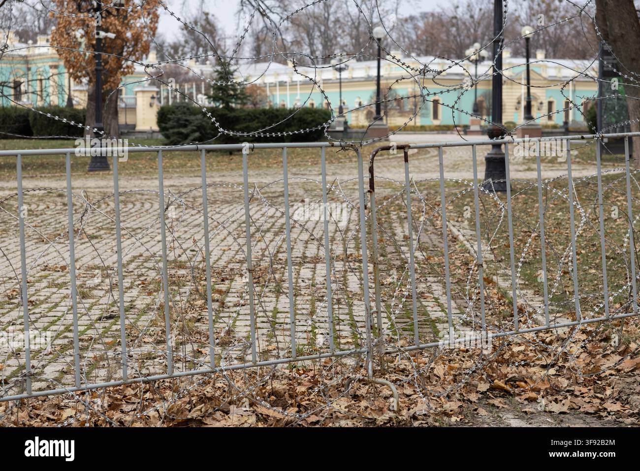 La pesante recinzione in acciaio avvolta da filo spinato pericoloso blocca l'ingresso di un parco pubblico, trasmettendo un'atmosfera di tensione, divieto e difesa p Foto Stock