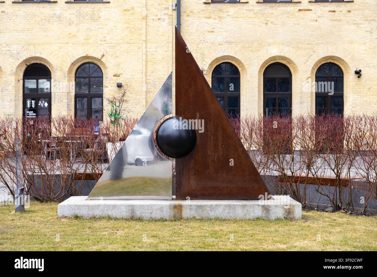 Kyiv, Ucraina - 22 marzo 2026: Installazione artistica moderna in metallo con un triangolo riflettente in acciaio e un segmento in ferro arrugginito con una sfera nera come punto focale Foto Stock