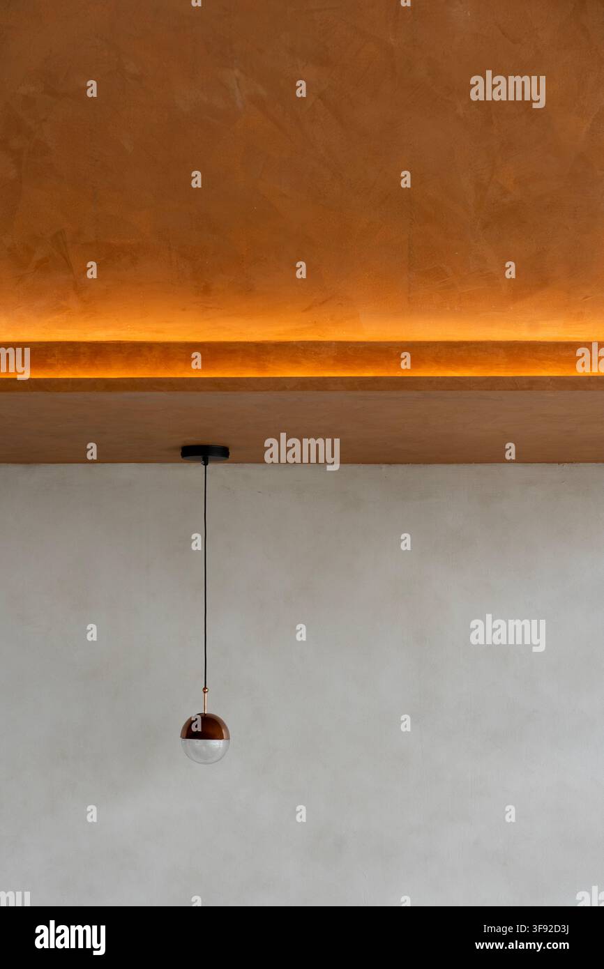 Dettaglio di interni minimalista che mostra un soffitto ruvido illuminato da una striscia luminosa calda lungo il bordo. Sotto il soffitto luminoso arancione caldo, Foto Stock